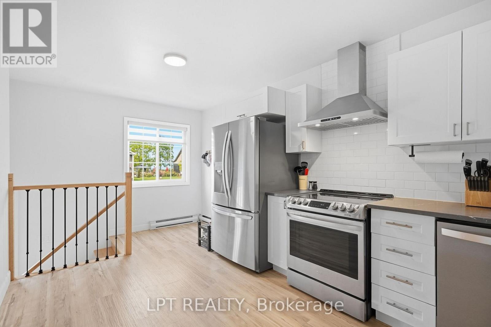 Modern kitchen with stainless steel appliances, white cabinetry, and a window overlooking greenery.