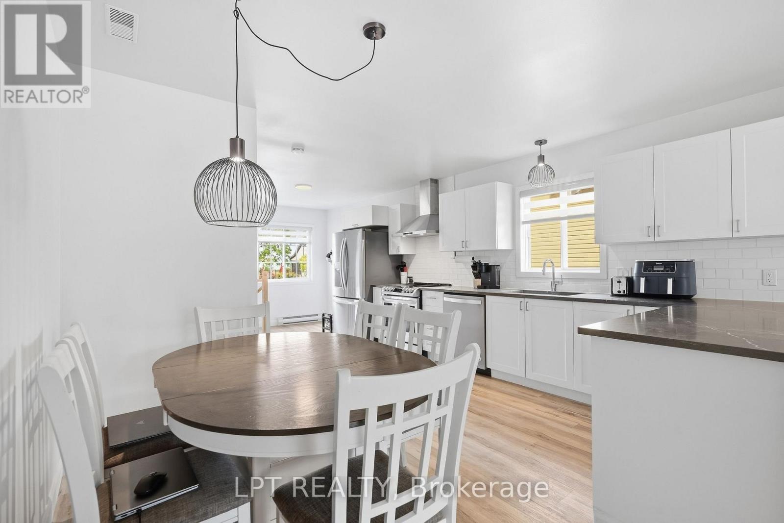 Bright white kitchen with stainless steel appliances, a dark countertop peninsula, and adjoining dining table.