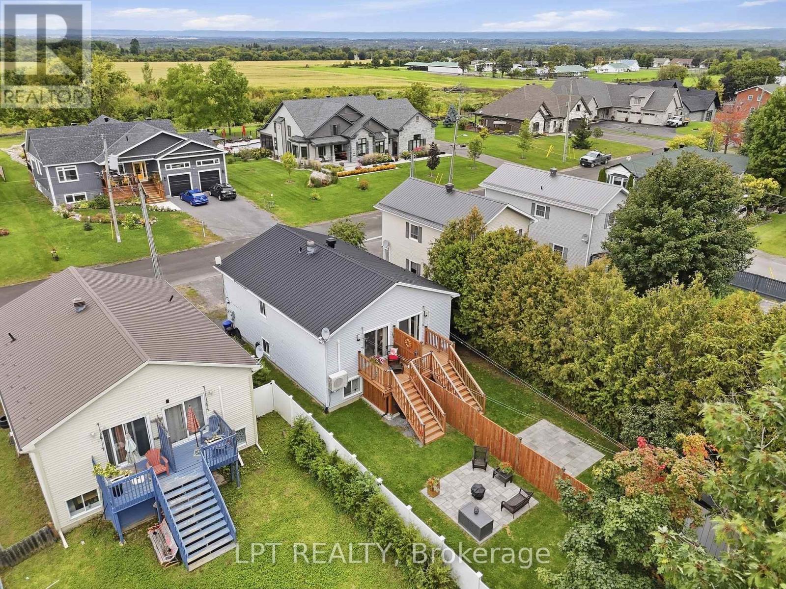 Aerial view of homes with fenced yards, raised decks and a paved patio, with fields in the distance.