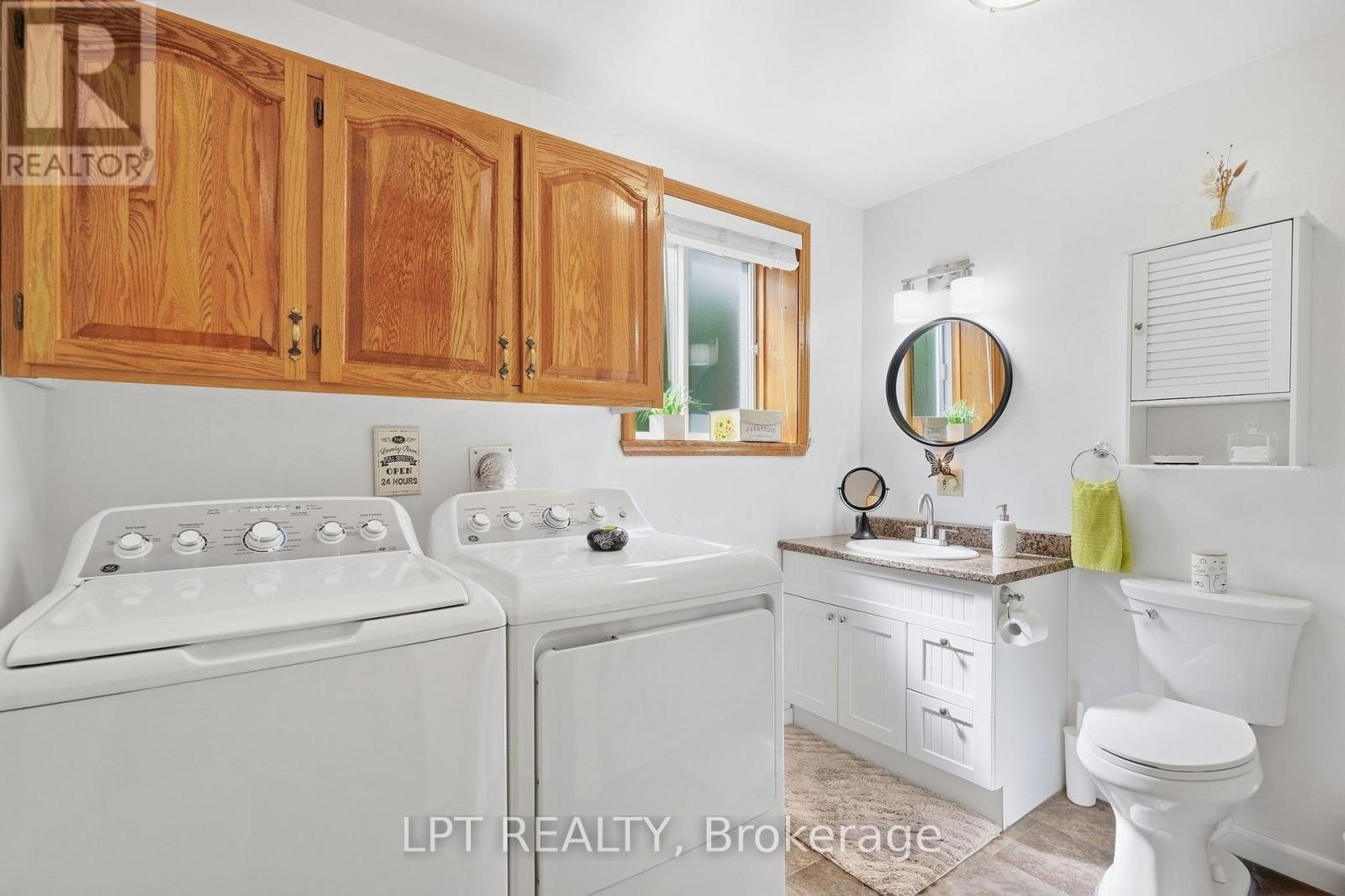 Bathroom laundry room with white washer and dryer, oak cabinets, vanity, and toilet.