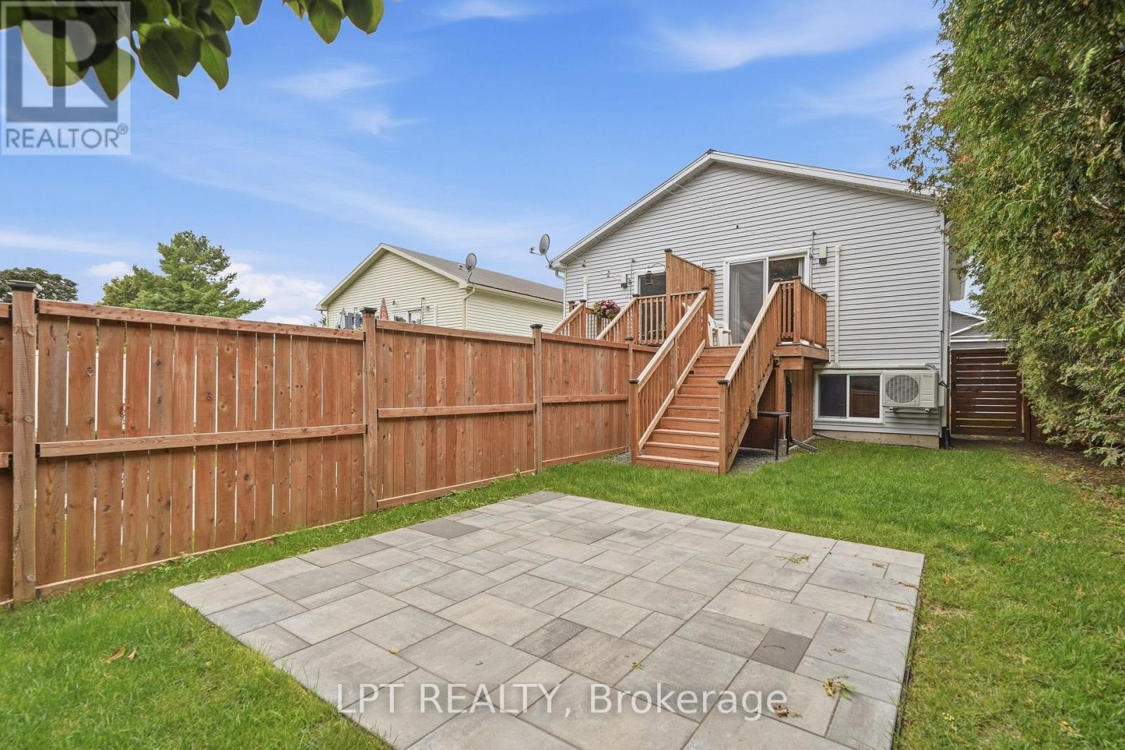 Backyard patio with a wooden privacy fence and raised deck beside a gray-sided house.