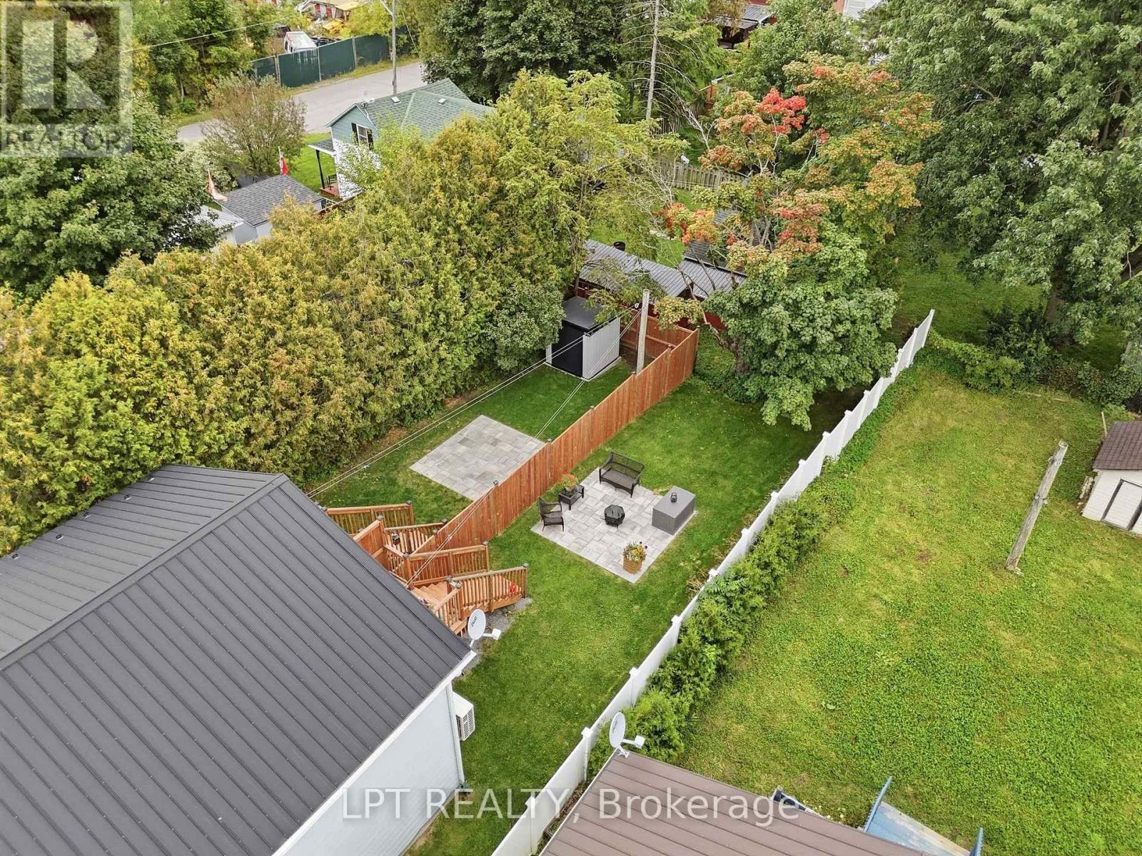 Aerial view of a fenced backyard with a stone patio, outdoor seating, deck and mature trees.