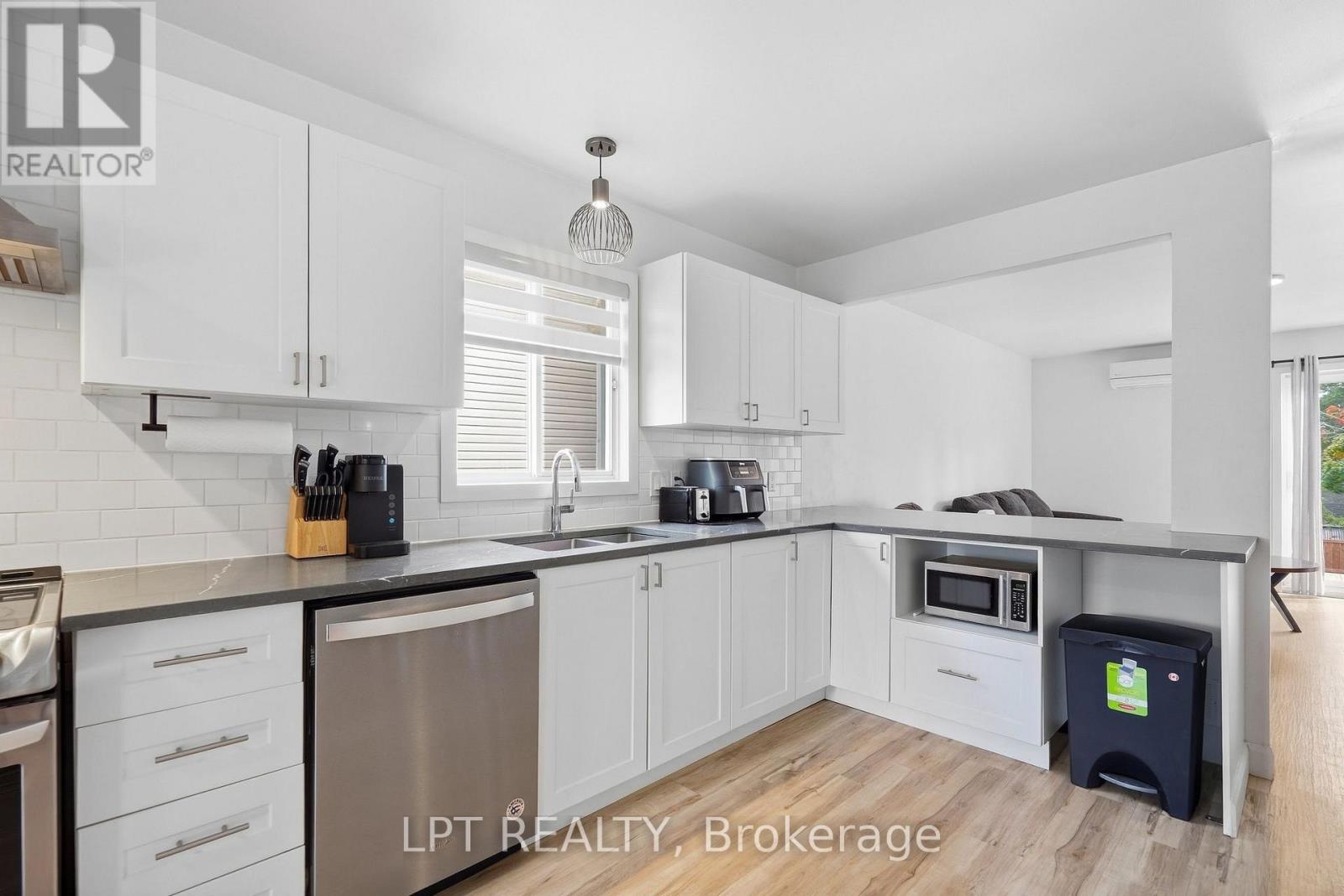 Modern white kitchen with gray counters, subway-tile backsplash, stainless dishwasher, and a peninsula with built-in microwave.