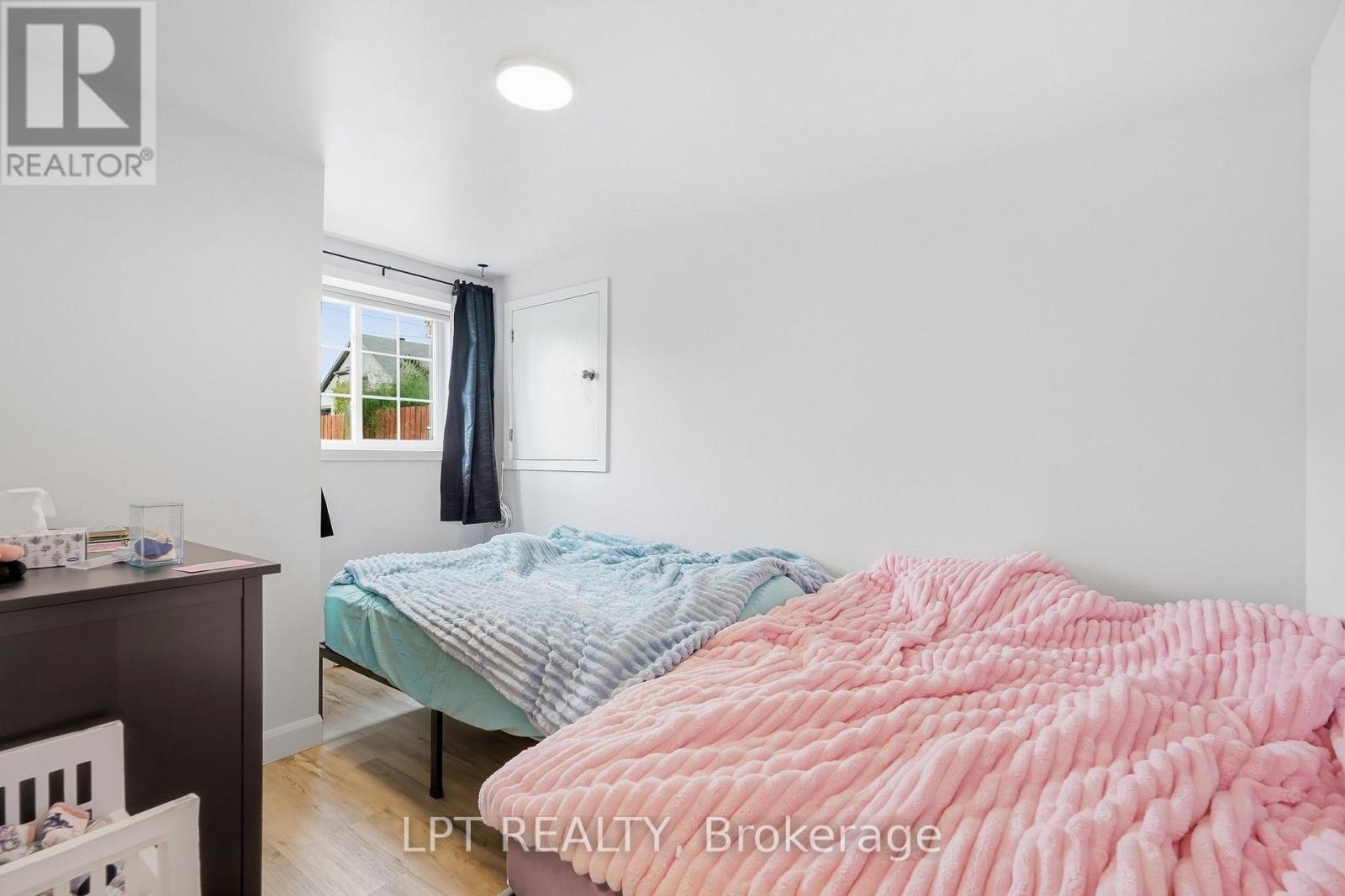Bedroom with two beds, pink and blue bedding, a curtained window, and light wood flooring.