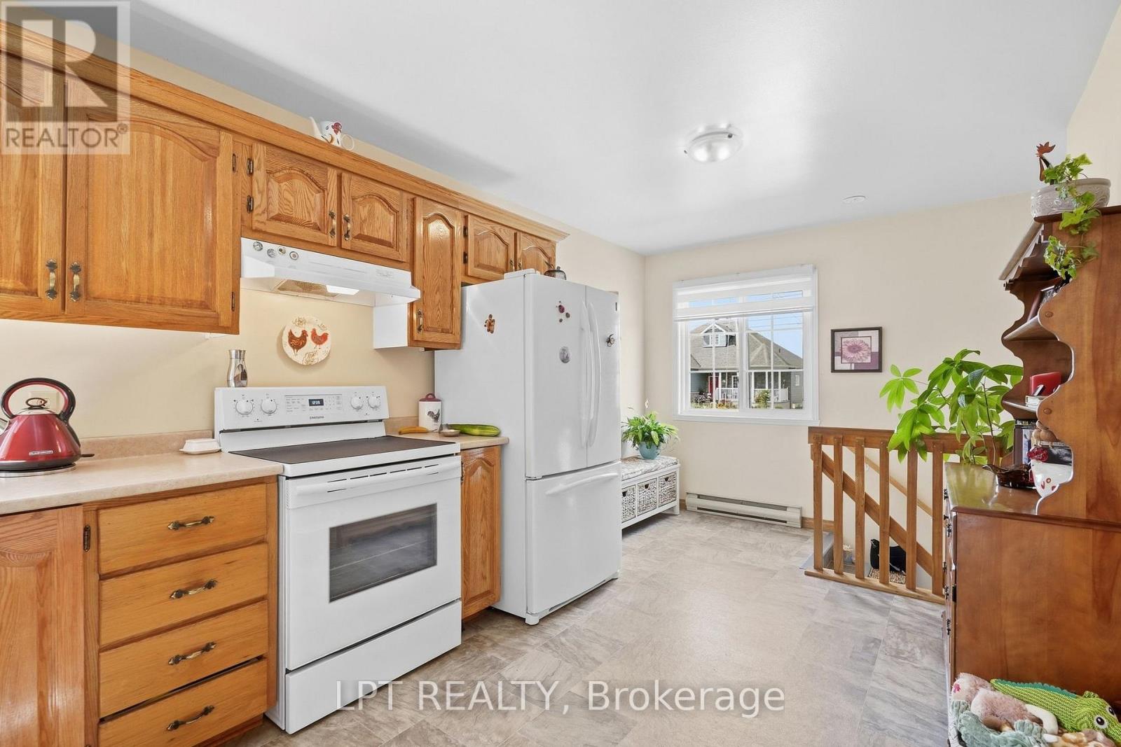 Kitchen with honey-colored wood cabinets, white appliances, and a window overlooking a neighboring house.