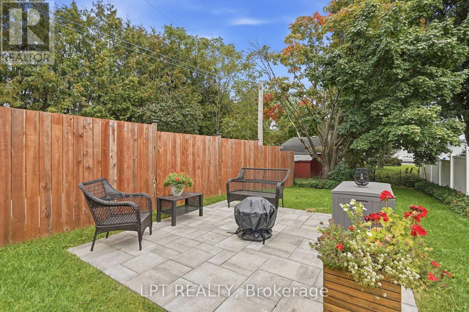 Backyard patio with stone pavers, wicker seating, wooden privacy fence, and flower planters.
