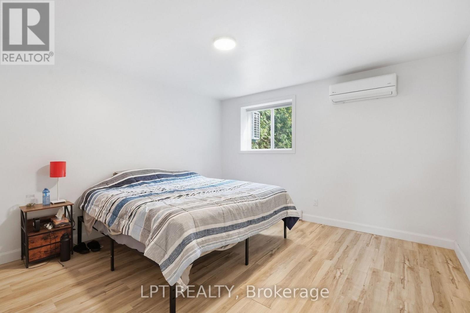 Bedroom with a striped bedspread, wood-look flooring, and a wall-mounted mini-split air conditioner.