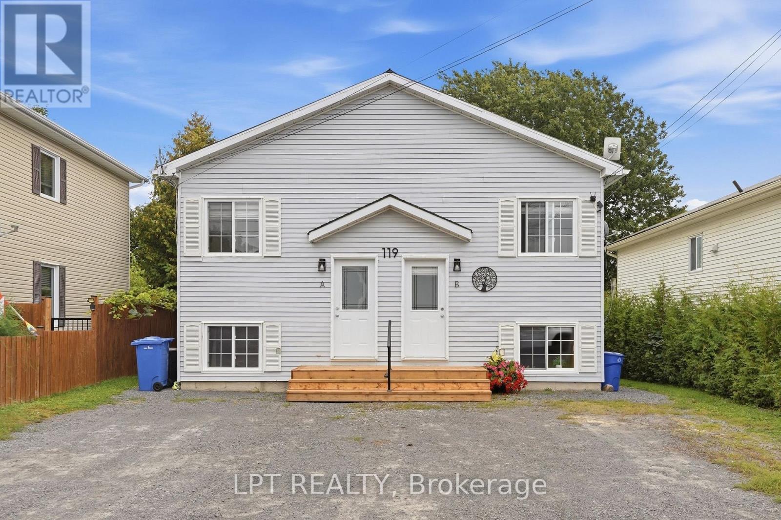 Gray-sided two-unit home with separate entrances, a raised wooden front step, and a gravel driveway.