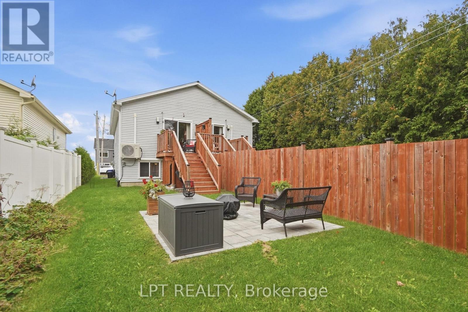 Rear yard with a paved patio, outdoor seating, wooden deck stairs, and privacy fencing.