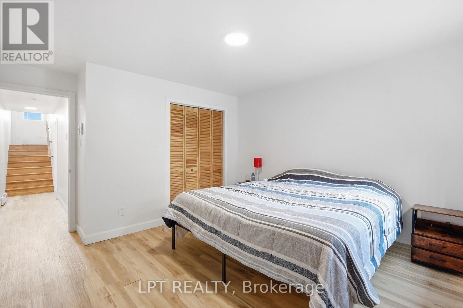 Bedroom with a striped bedspread, wooden louvered closet doors, and a hallway leading to stairs.