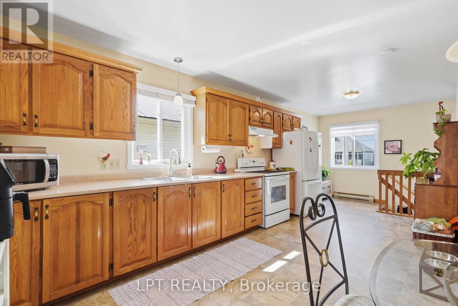 Kitchen with honey-colored wood cabinets, white appliances, and a dining area by the window.