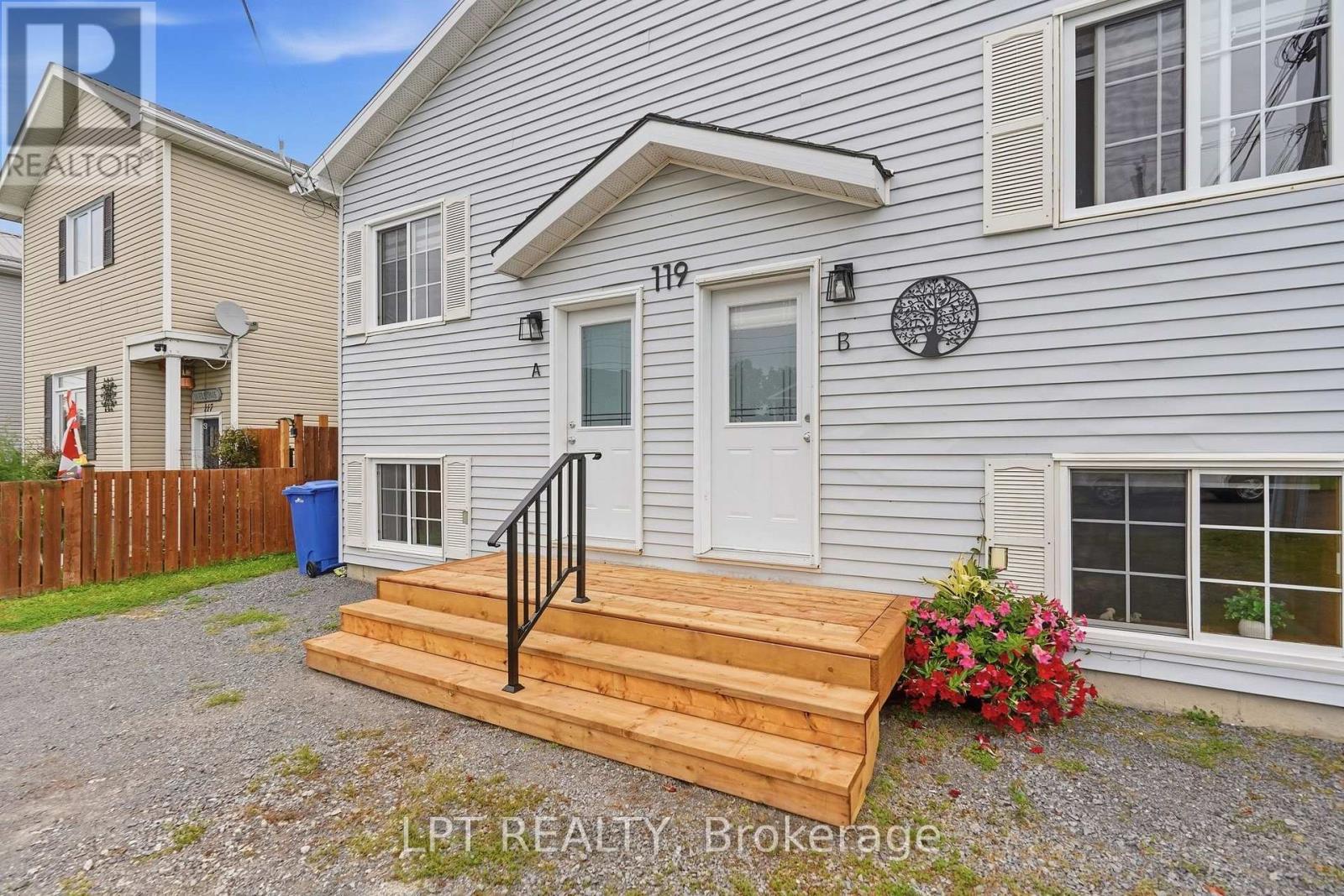 Gray-sided home with two entry doors and a broad wooden deck with black railing.