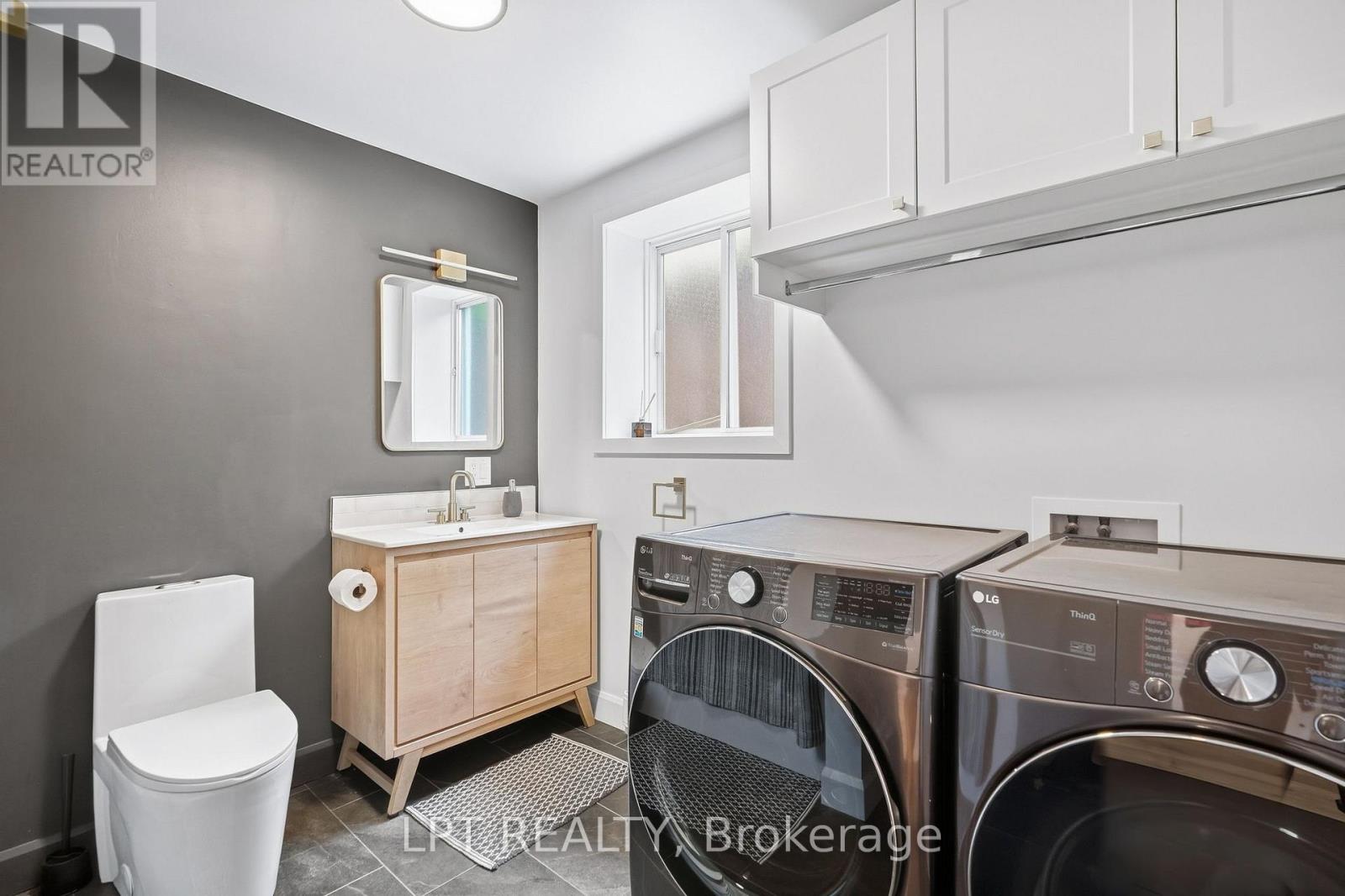 Bathroom and laundry room with a wood vanity, toilet, and front-loading washer and dryer.
