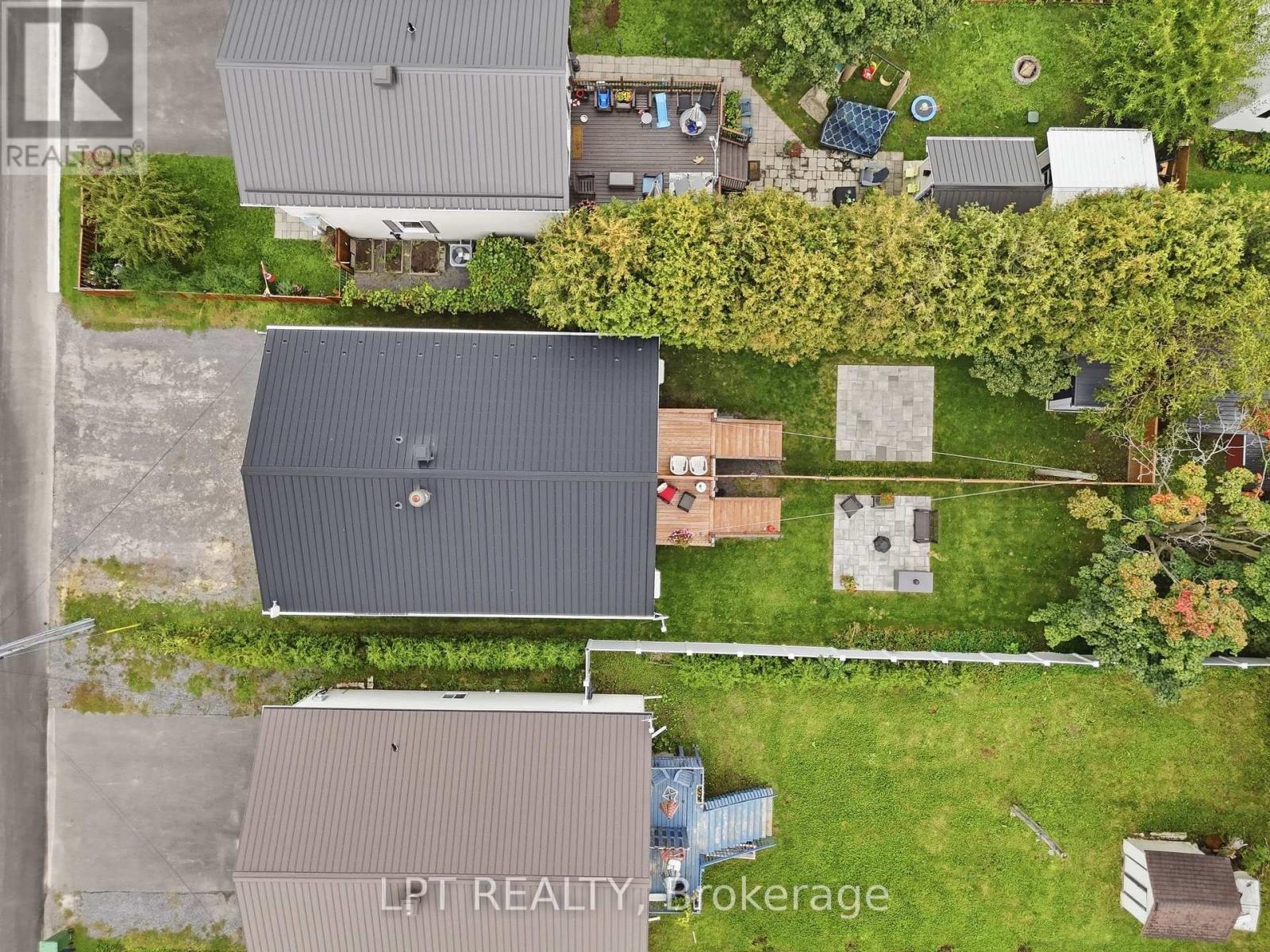 Aerial view of a metal-roofed home with a green yard, wooden decks, and paved patios.