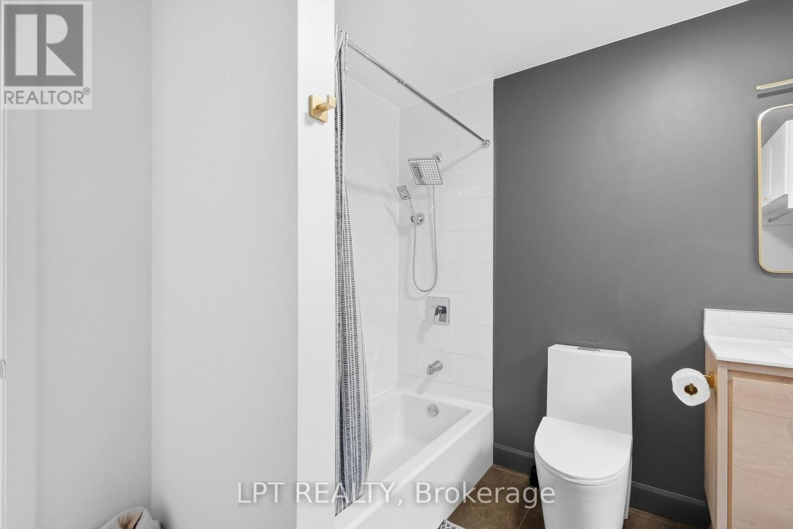 Bathroom with a tiled tub and shower, modern toilet, and light wood vanity.