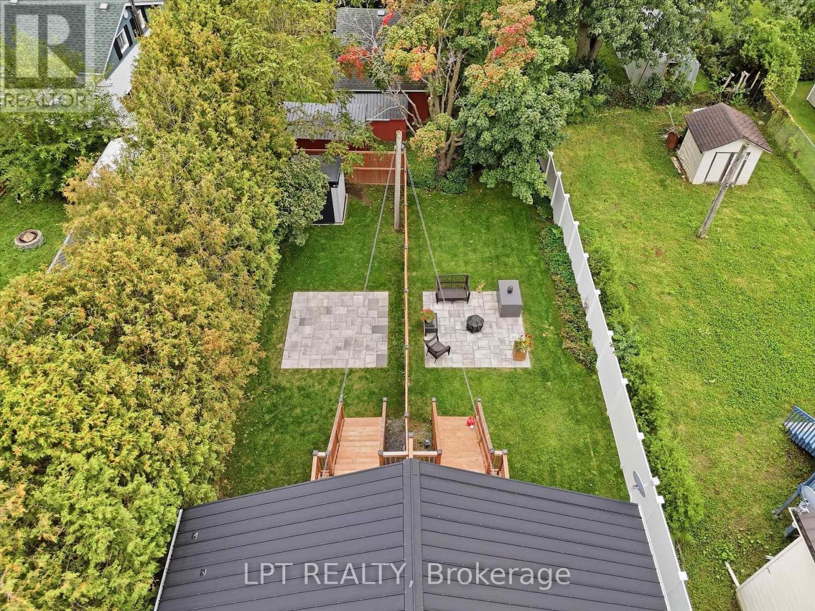 Aerial view of a fenced backyard with a paved patio, fire pit, shed, and mature trees.