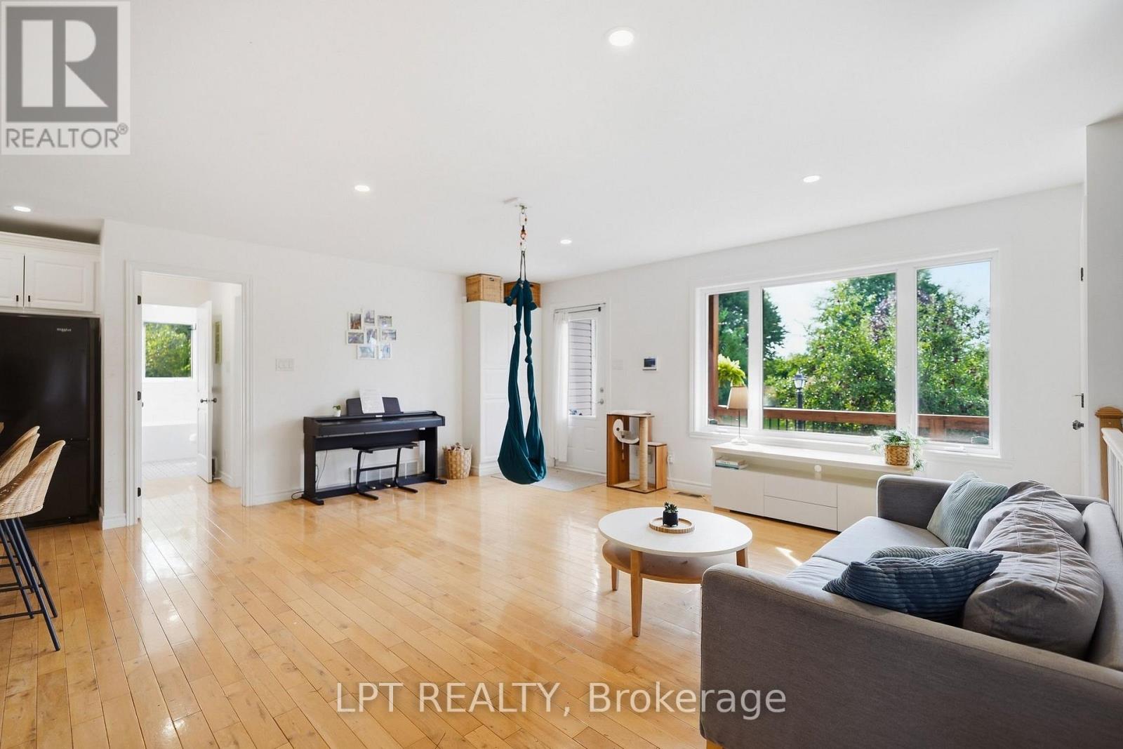 Bright living room with hardwood floors, a gray sectional, large garden-facing windows, and a hanging chair.