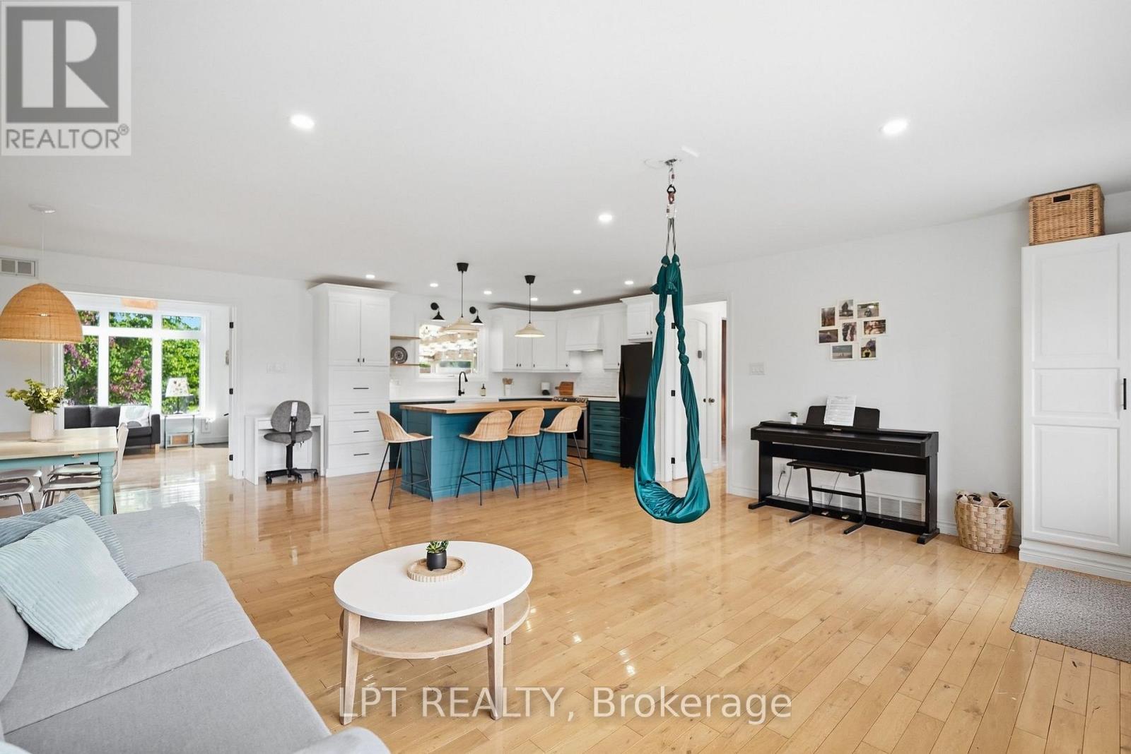 Open-concept living room and kitchen with a teal island, hardwood floors and a hanging chair.
