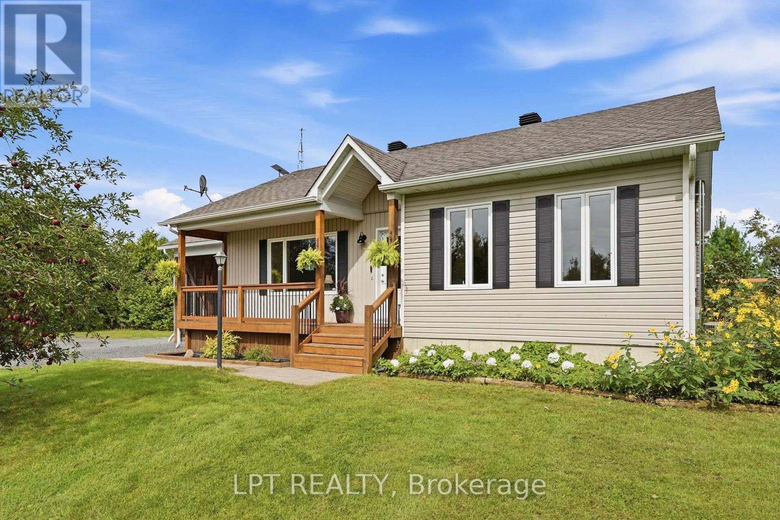 Single-storey beige home with a covered wooden porch, dark shutters, and flower gardens.
