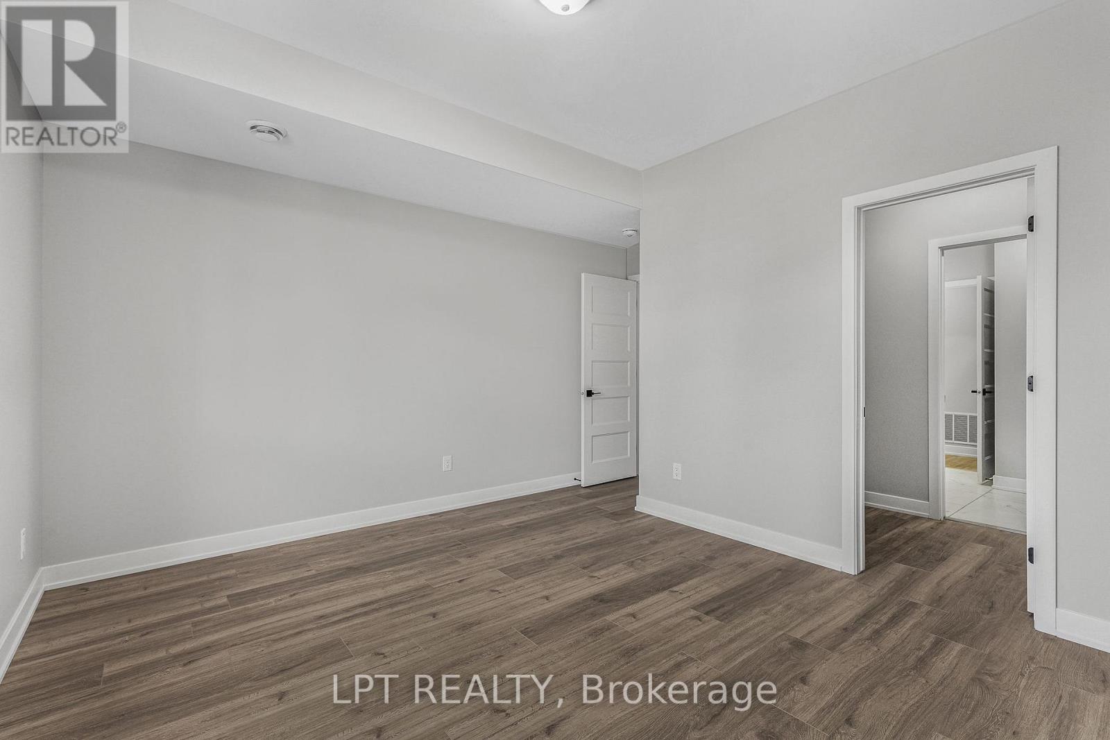 Empty room with brown wood-look flooring and open doorways to adjoining spaces.