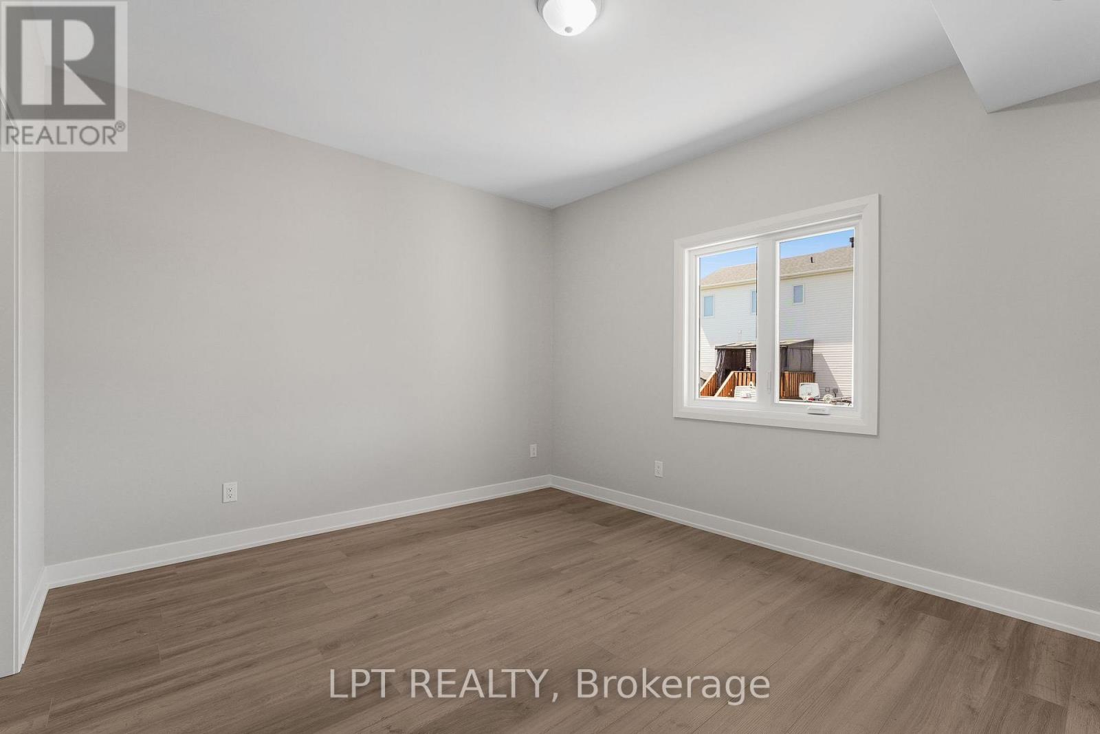 Empty room with gray walls, wood-look flooring, and a window overlooking neighboring homes.