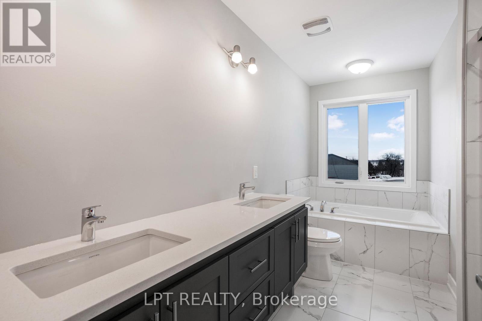 Modern bathroom with a dark double vanity, marble-look tile, and a bathtub beneath a window.