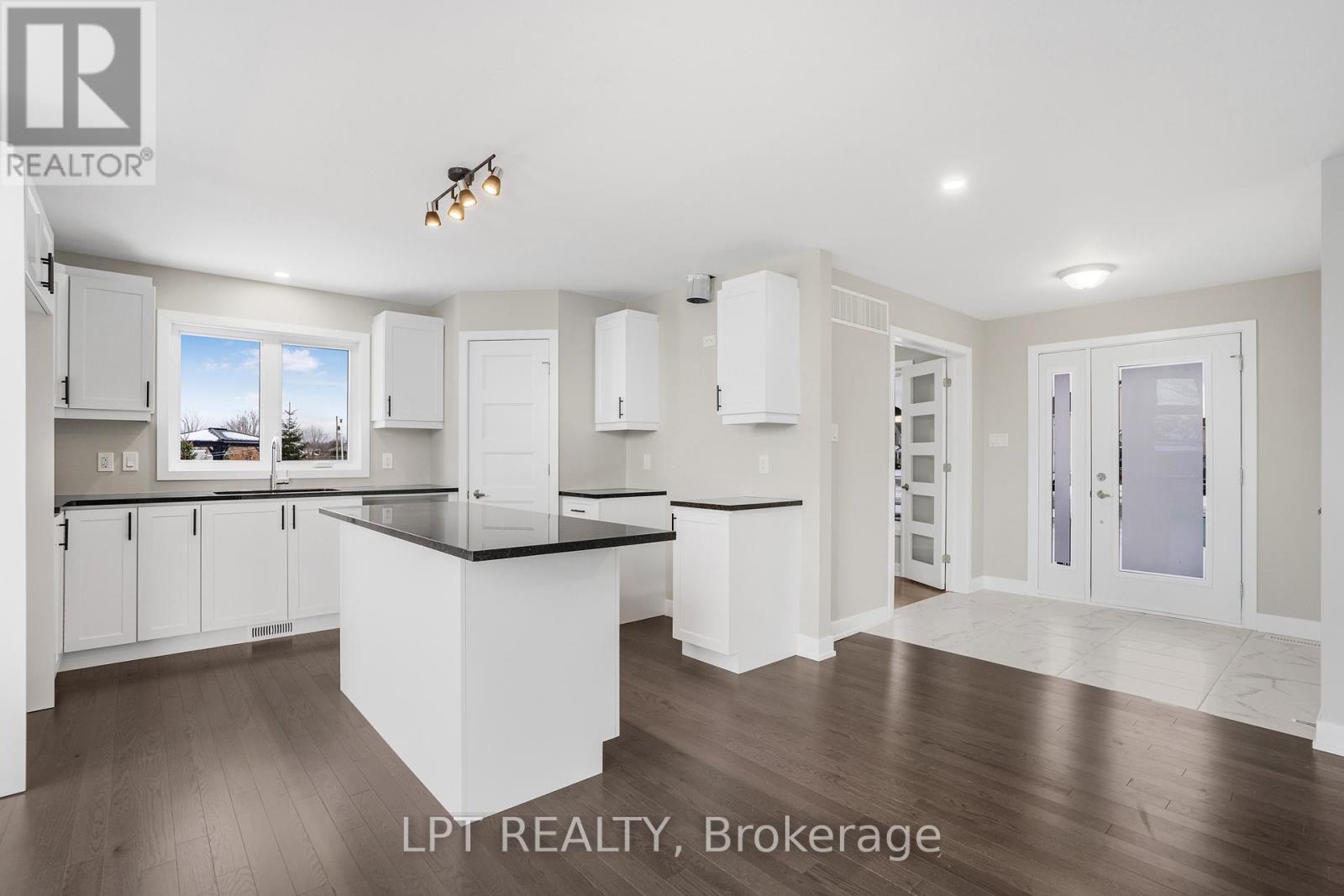 Kitchen with white cabinets, a dark-countertop island, and wood floors.