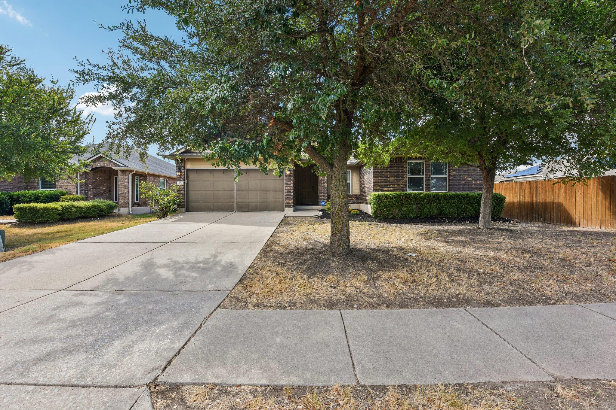 Single-story brick home with a double garage and wide driveway beneath mature shade trees.