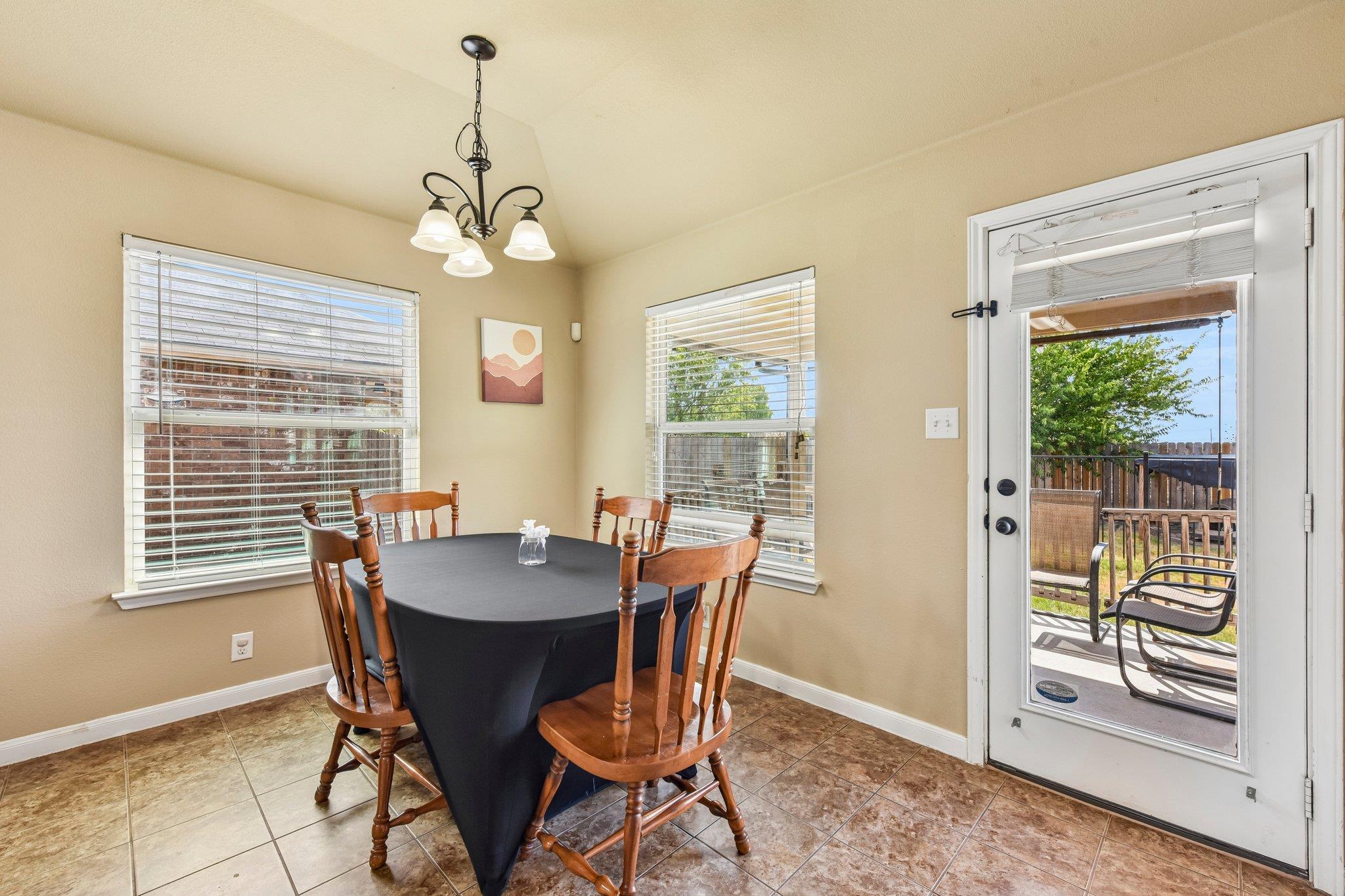 Dining area with a dark table and wooden chairs beside a glass door opening to a fenced patio.