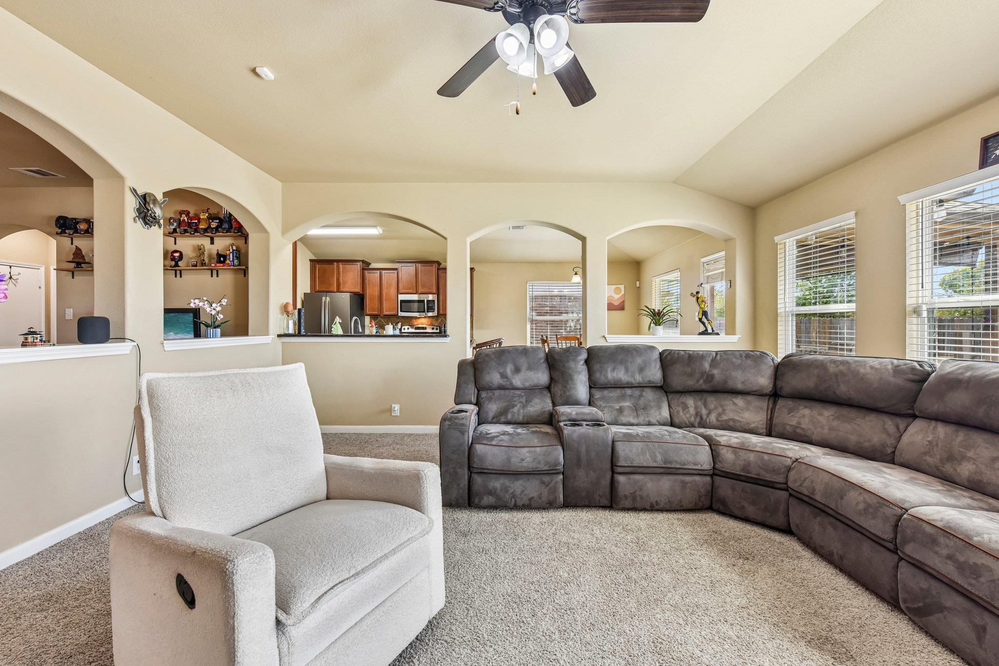 Living room with a gray sectional, white armchair, arched openings, and views into the kitchen.