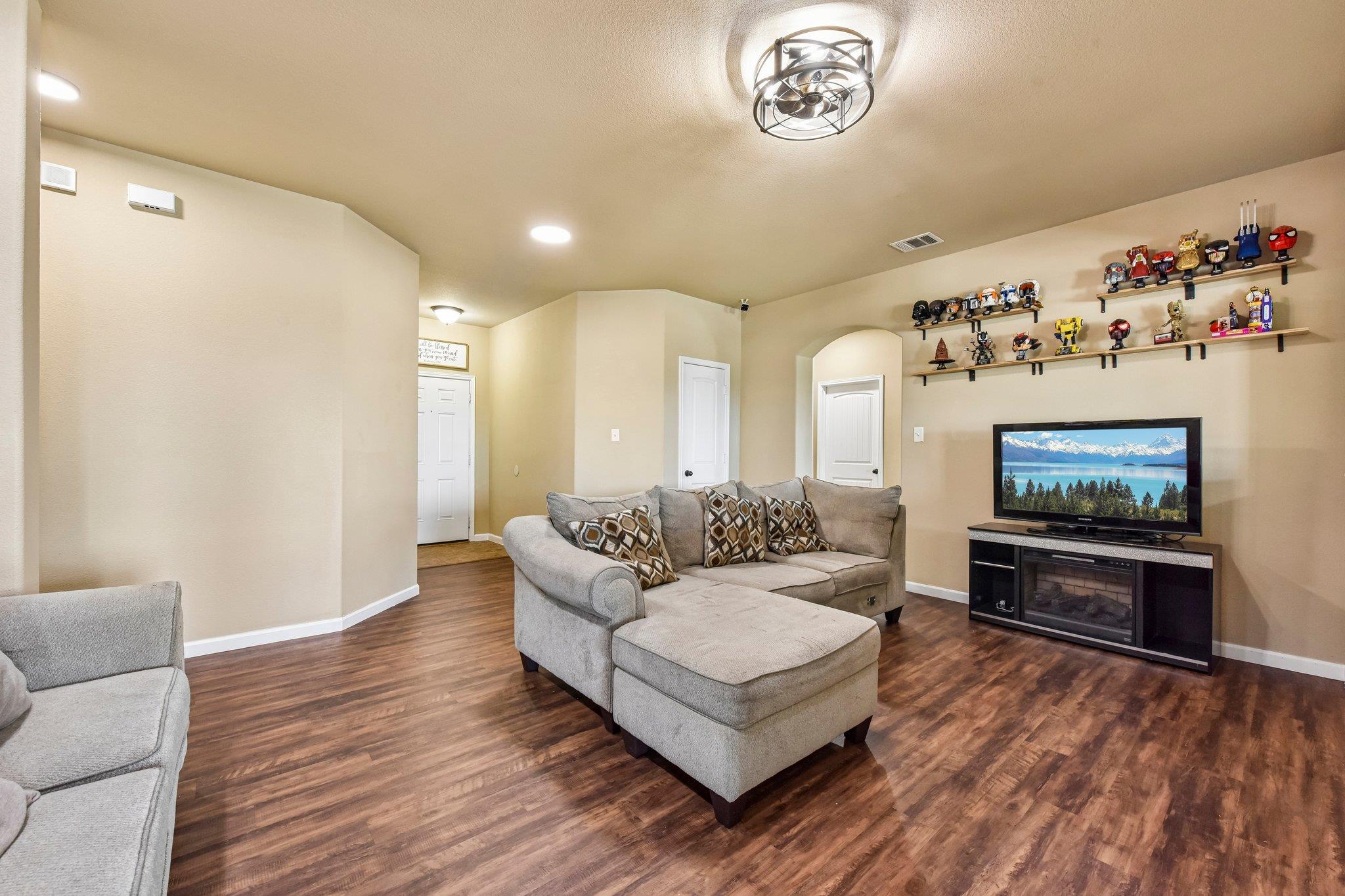 Furnished living room with a gray sectional, ottoman, television, and shelves of collectibles.