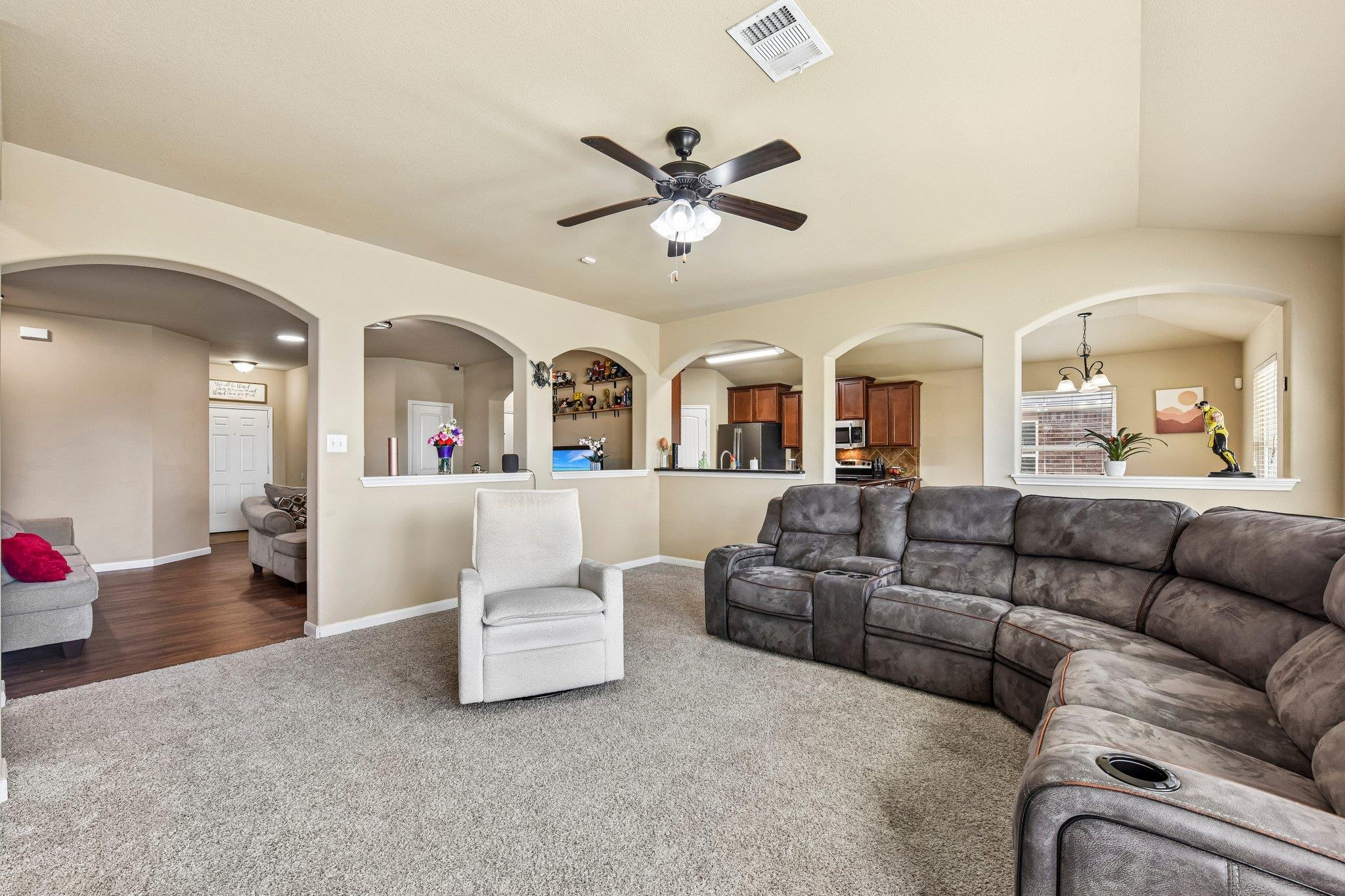 Living room with a gray sectional, light carpet, ceiling fan, and arched openings to adjacent rooms.