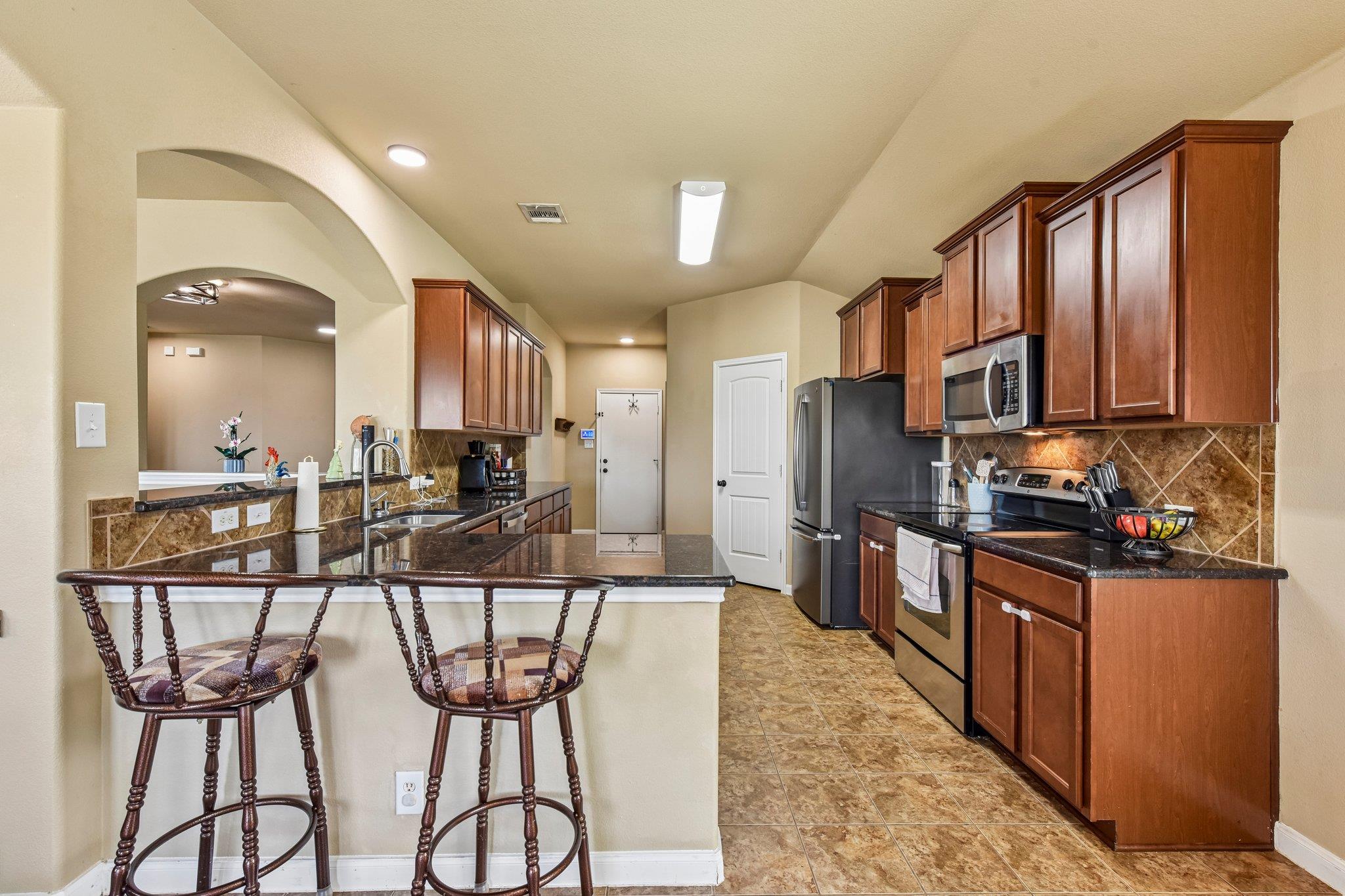 Kitchen with dark wood cabinetry, granite counters, breakfast bar, and stainless steel appliances.