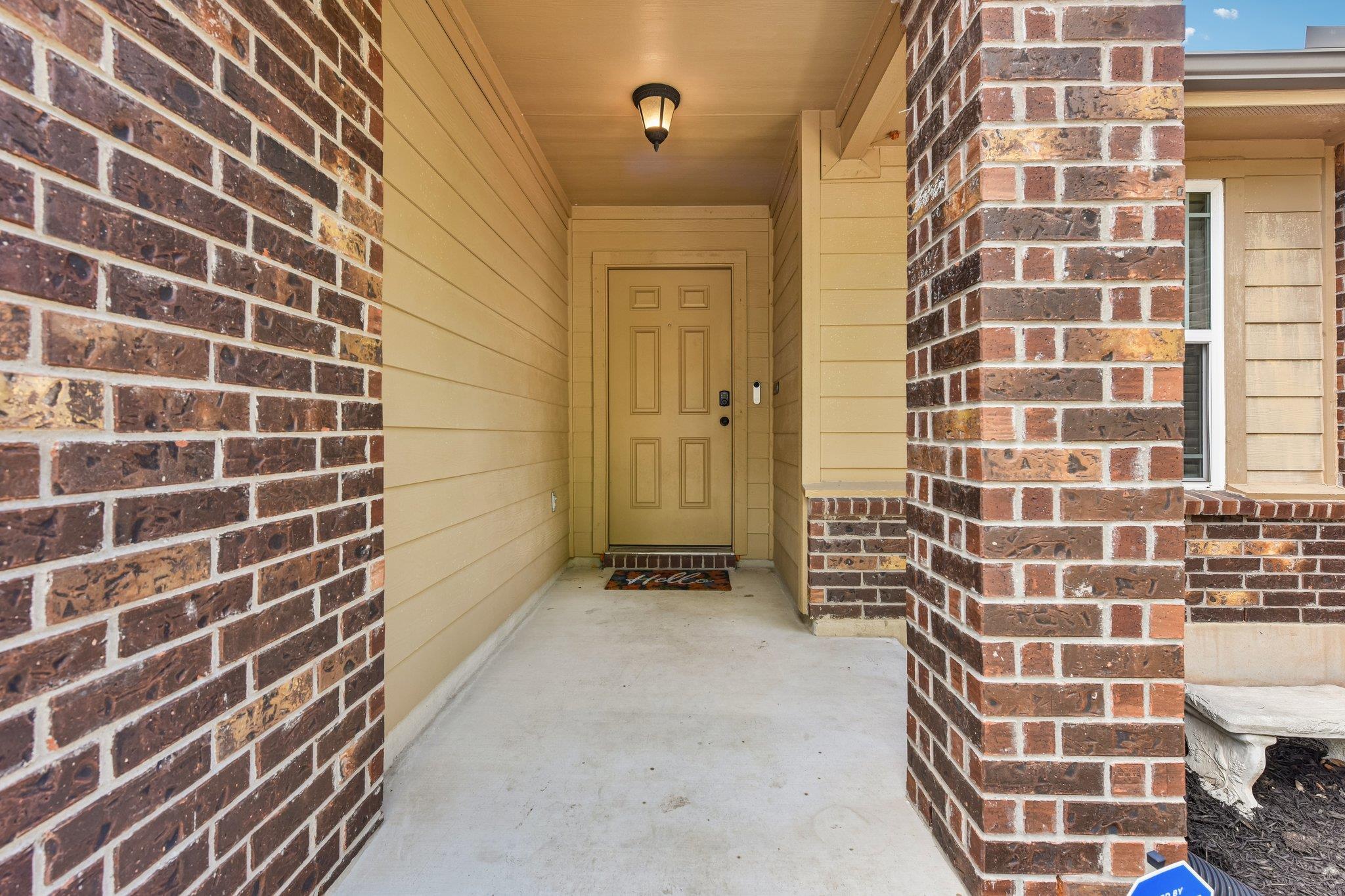 Covered front entry with a tan door, brick columns, and overhead porch light.