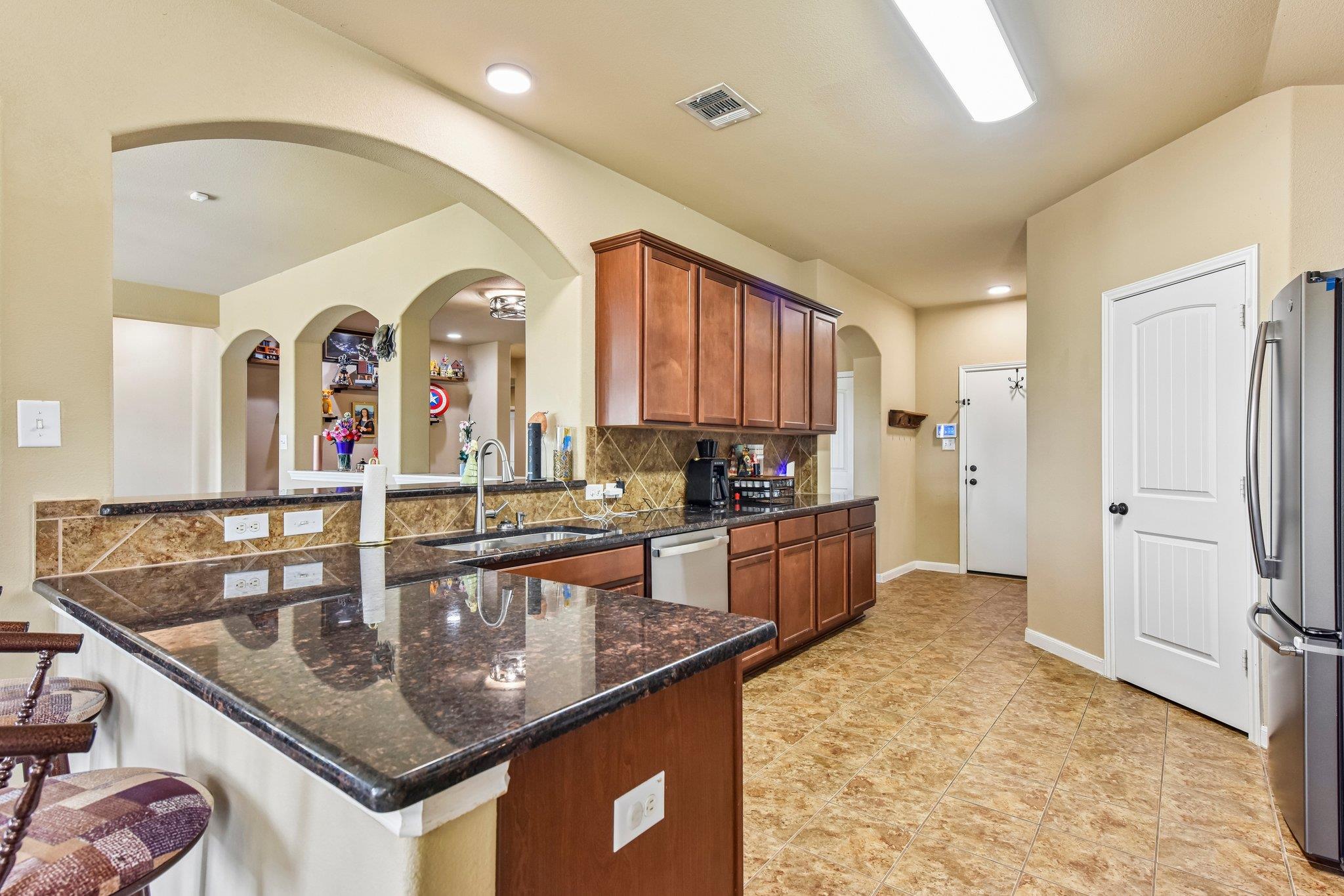 Kitchen with dark granite counters, reddish-brown cabinets, and arched openings to adjacent rooms.