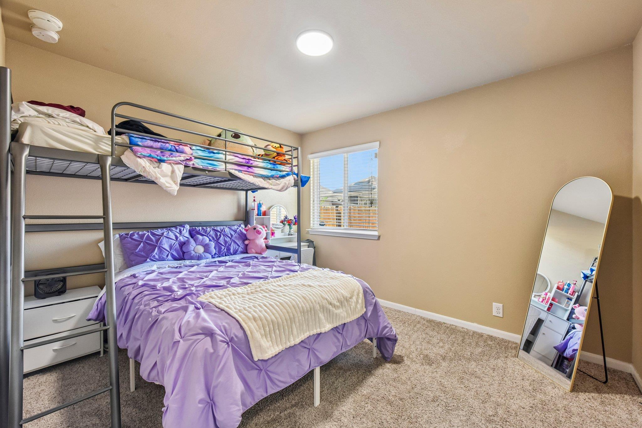 Bedroom with a metal bunk bed, purple bedding, plush toys, and a leaning full-length mirror.