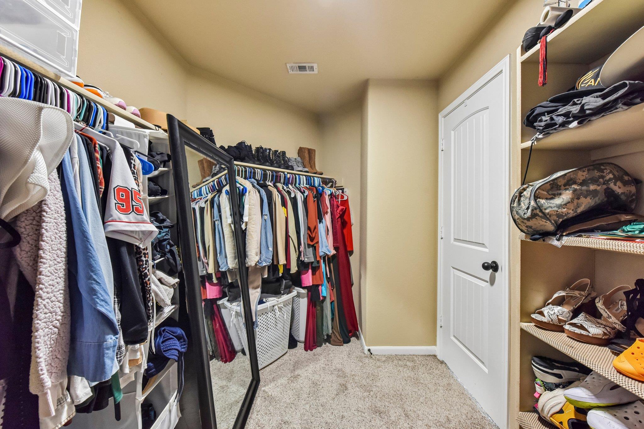 Walk-in closet with clothing racks, built-in shoe shelves, laundry baskets, and a full-length mirror.