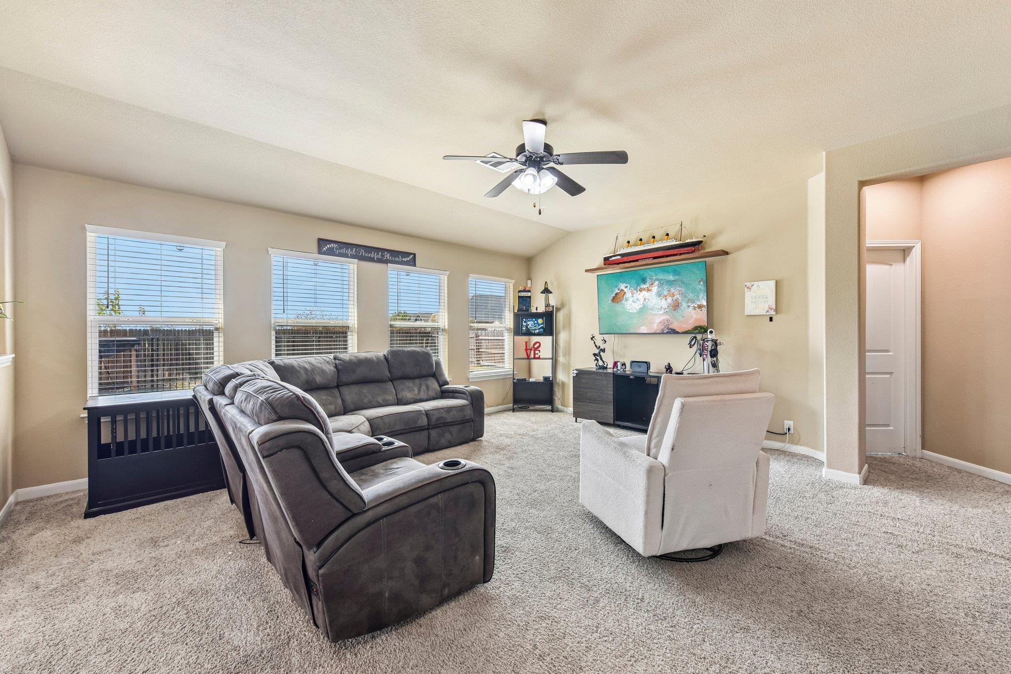 Furnished living room with gray reclining sectional, white armchair, and windows with blinds.