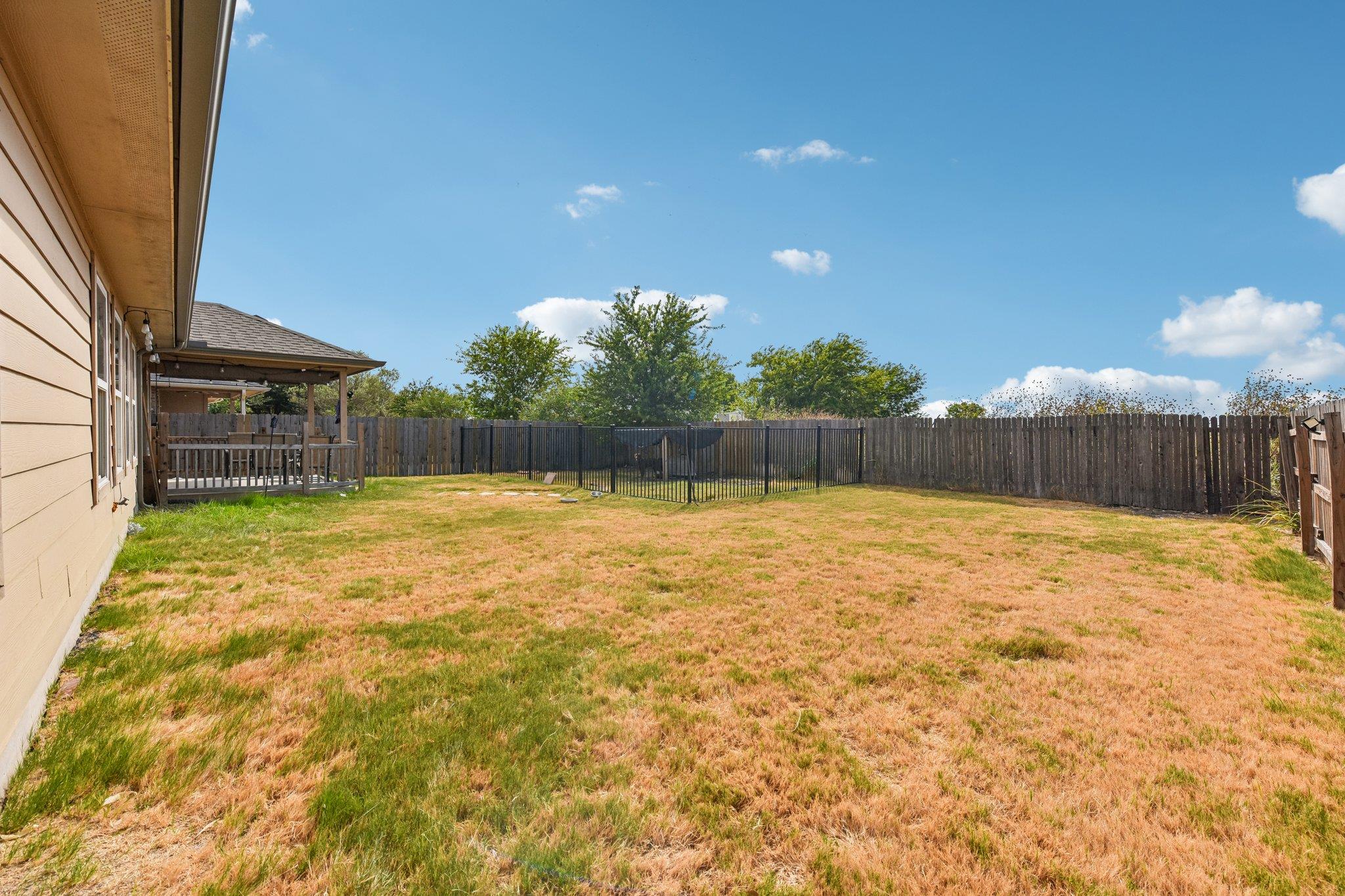 Backyard with a covered patio, wooden privacy fence, and black metal fenced area.