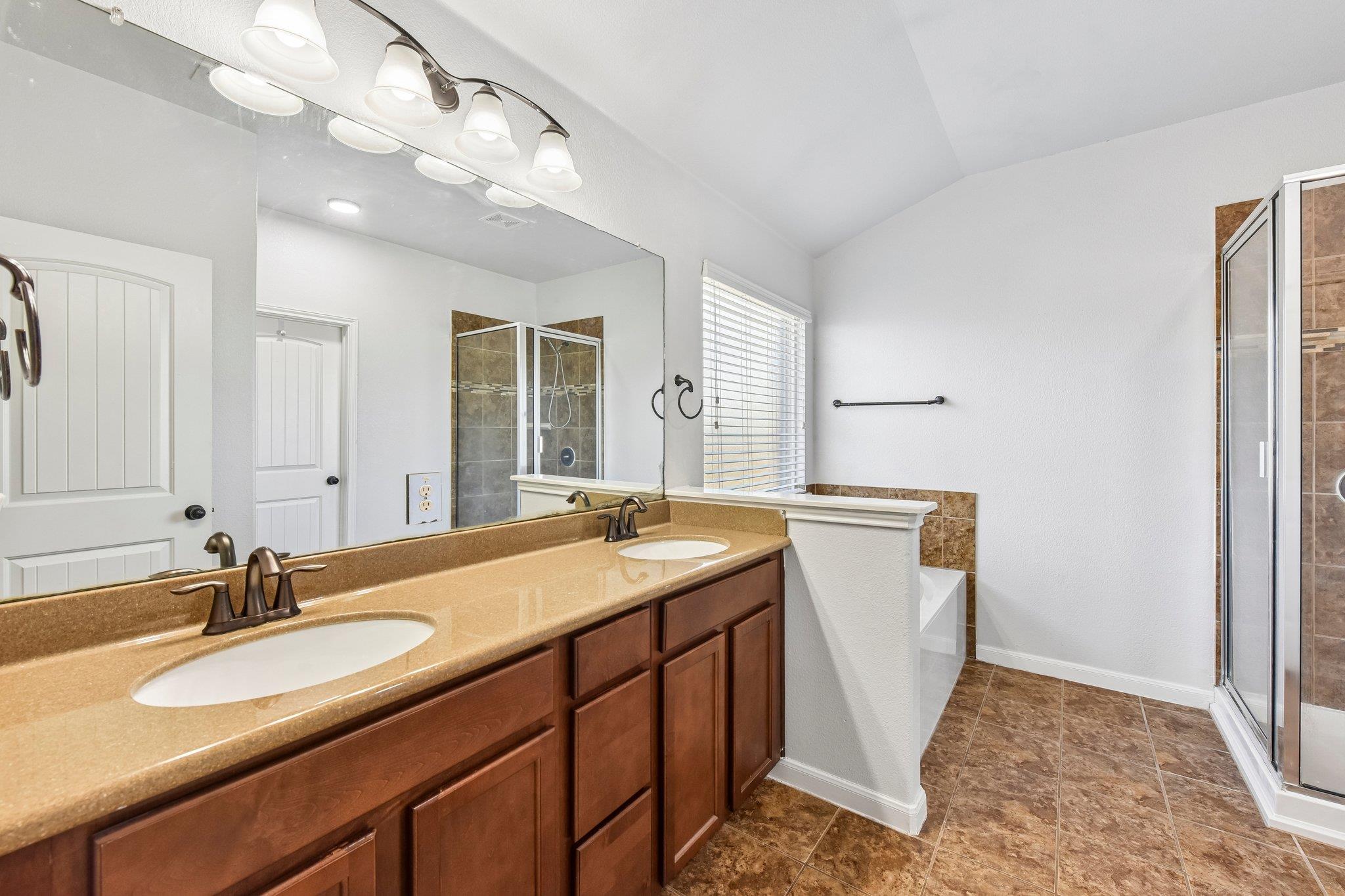 Bathroom with a double-sink vanity, large mirror, tiled floor, and glass-enclosed shower.