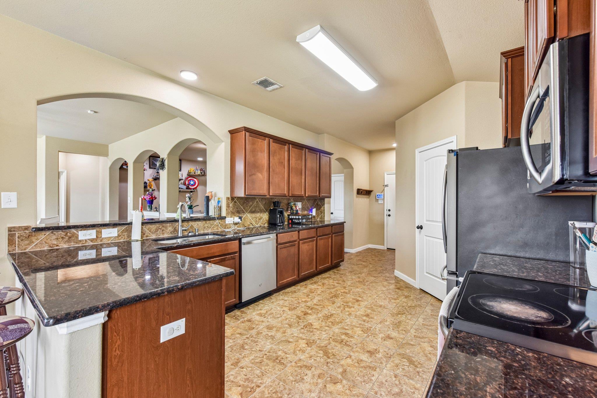 Kitchen with reddish wood cabinets, granite counters, a breakfast bar, and patterned tile floors.