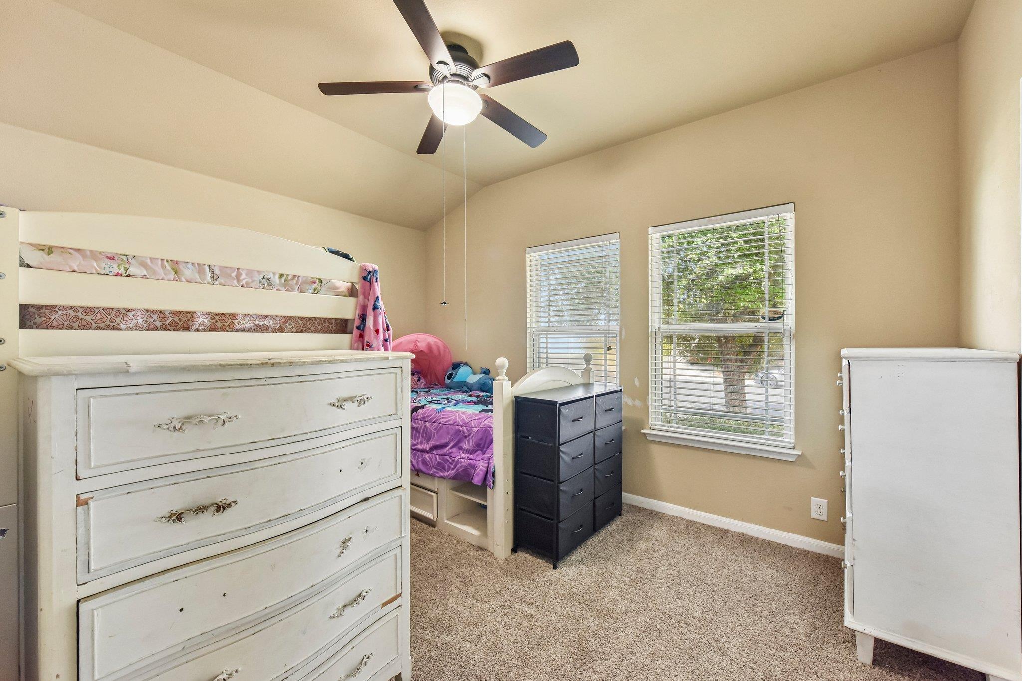 Bedroom with a white bunk bed, large dresser, ceiling fan, and two windows with blinds.