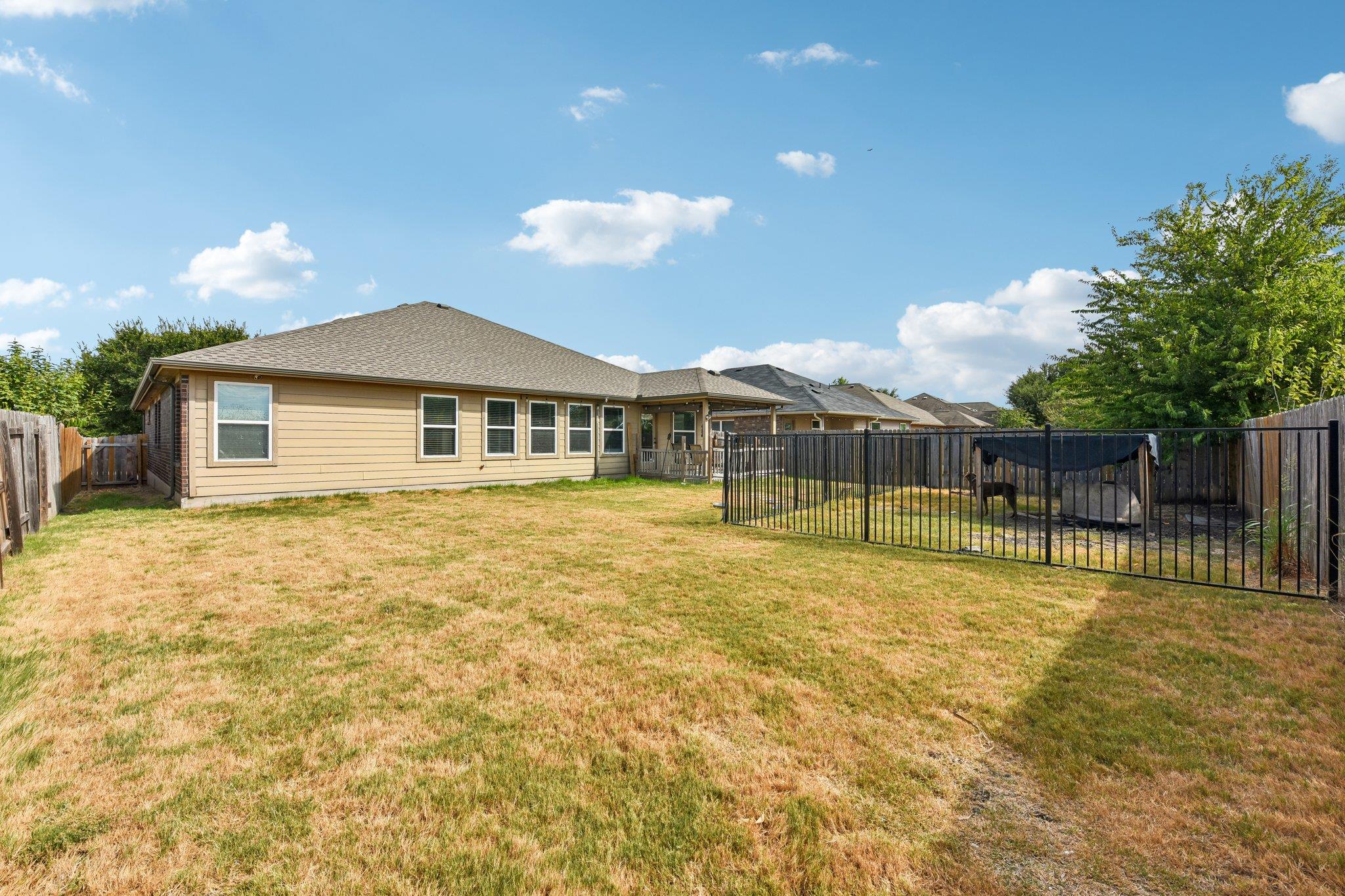Rear of a tan single-story house beyond a dry lawn, with a fenced enclosure in the backyard.
