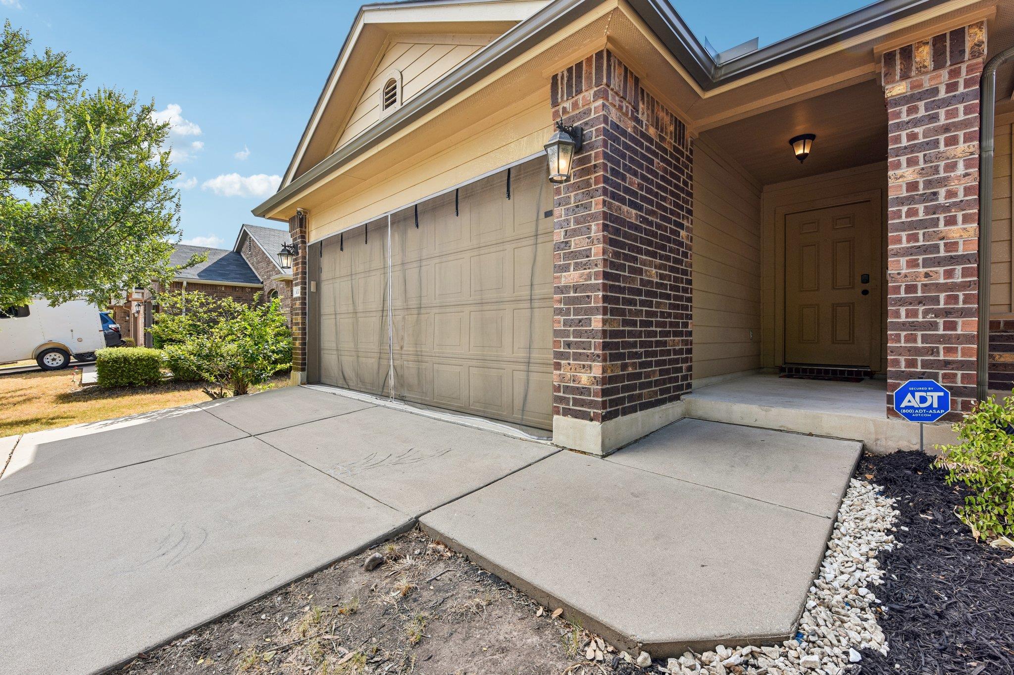 Home exterior with a wide garage door and covered brick entry beside the concrete driveway.