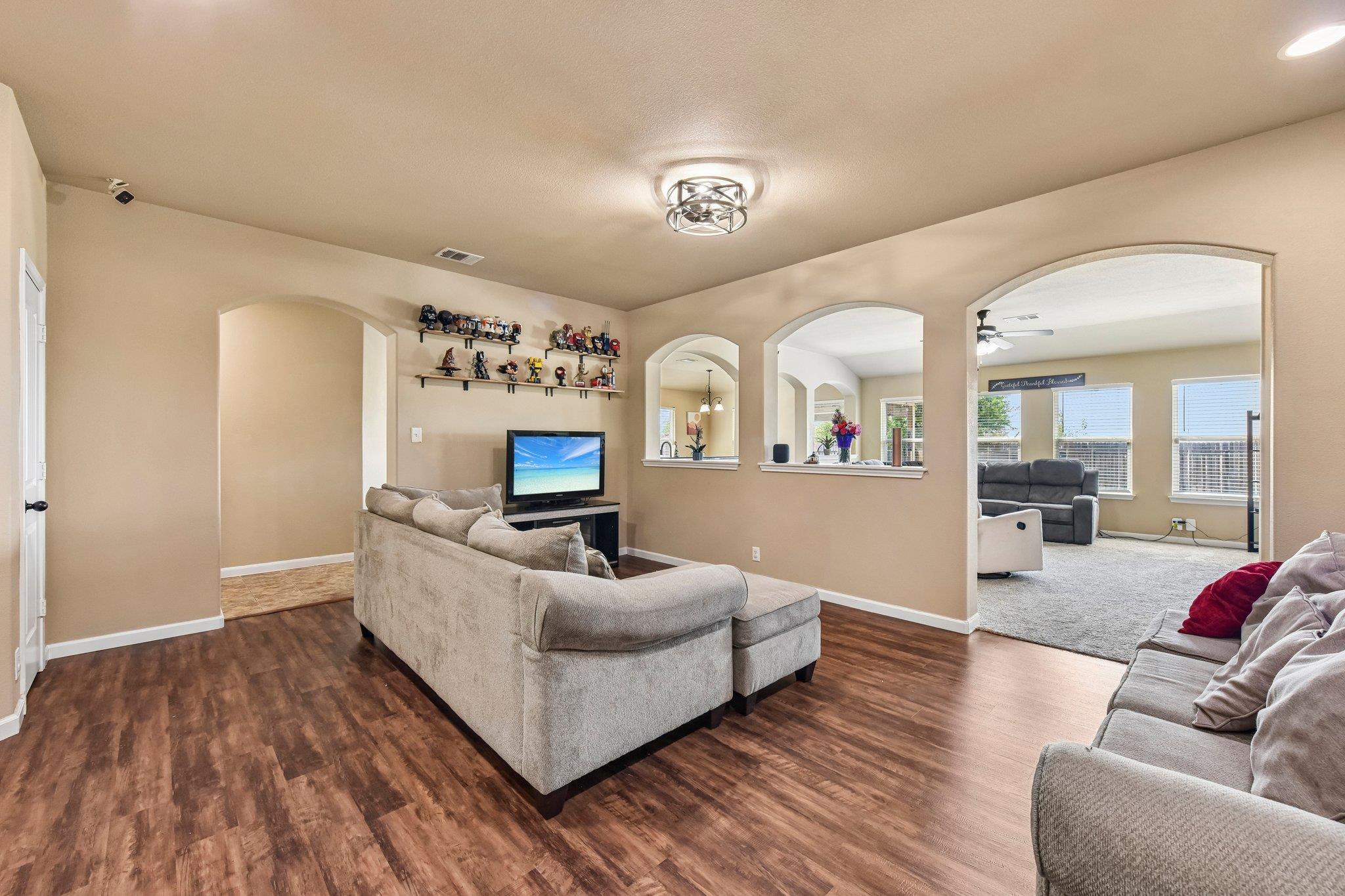 Furnished living room with gray sectional sofas, wood-look floors, and arched openings to an adjacent sitting area.