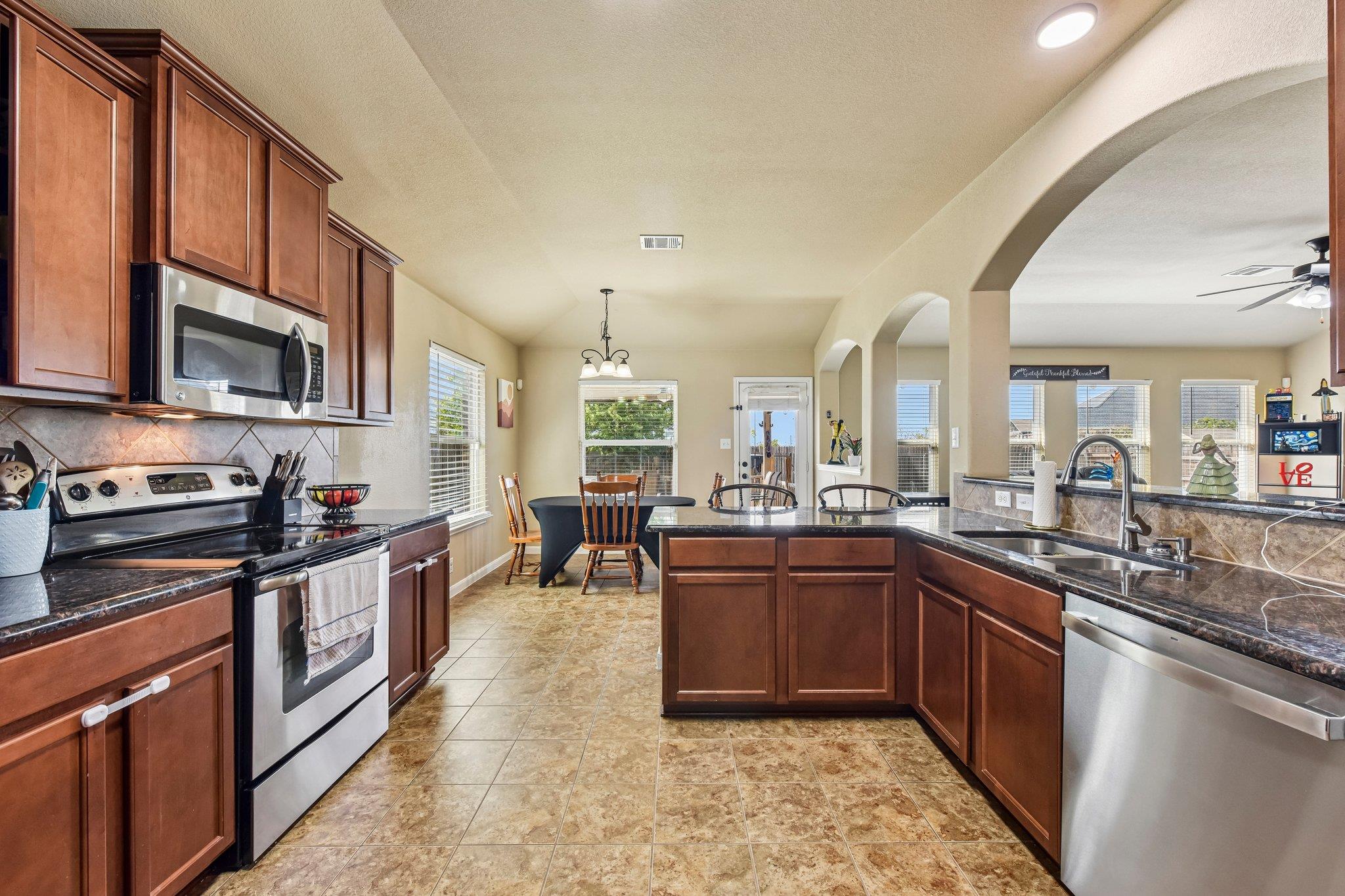 Kitchen with dark wood cabinets, granite counters, stainless steel appliances, and a central island opening to a dining area.