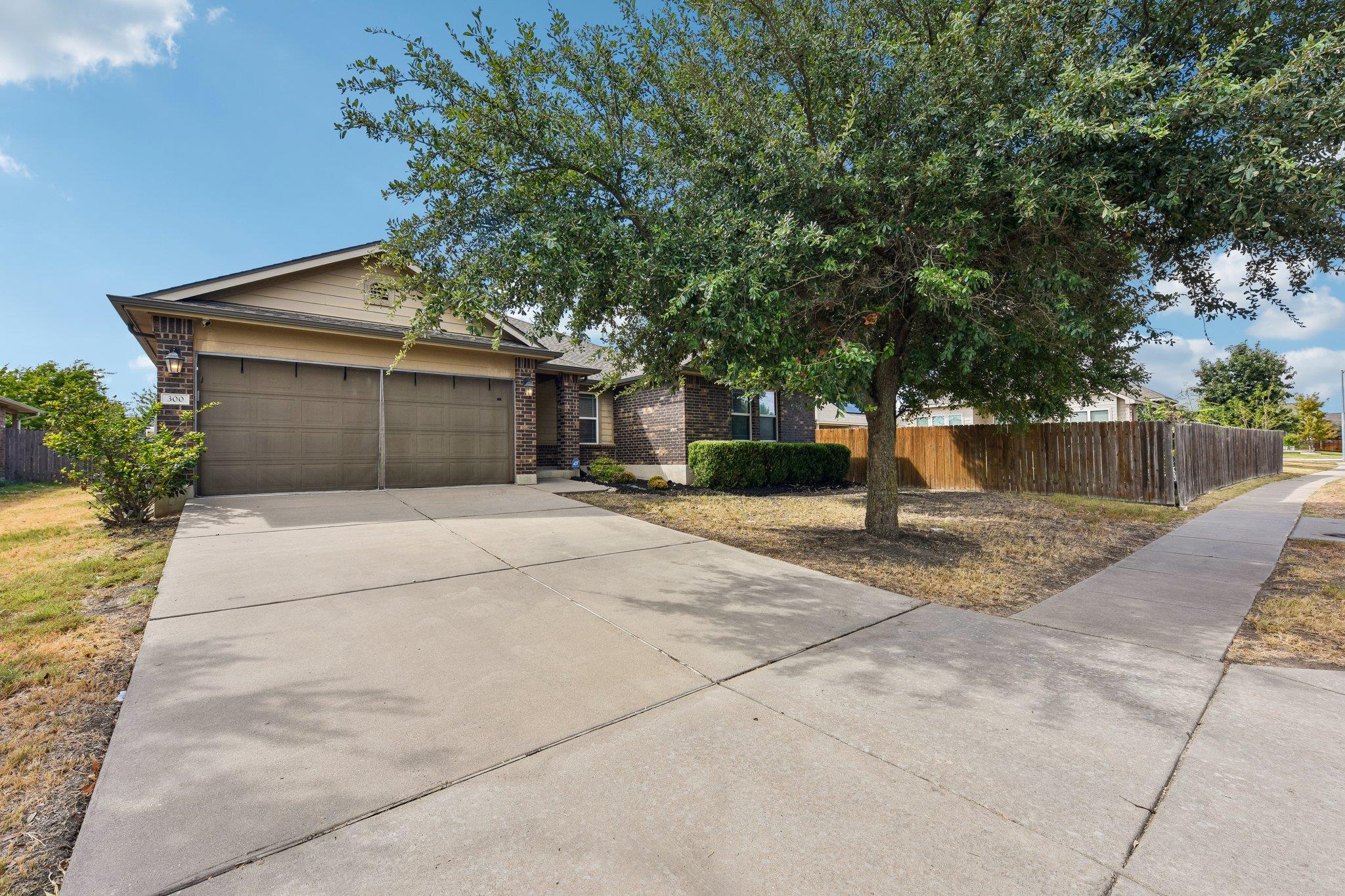 Single-story brick home with a double garage, broad driveway, and large shade tree.