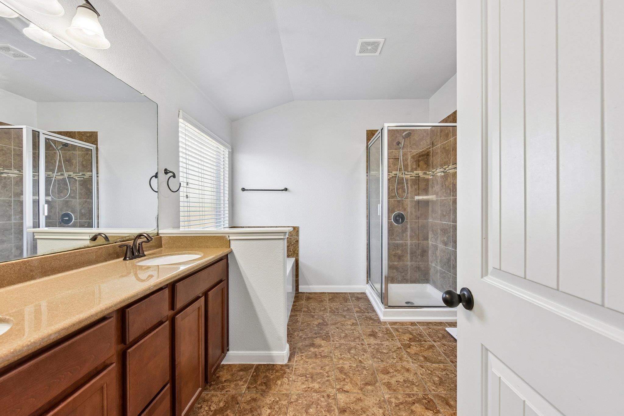 Bathroom with a wood vanity and tan counter beside a glass-enclosed tiled shower.