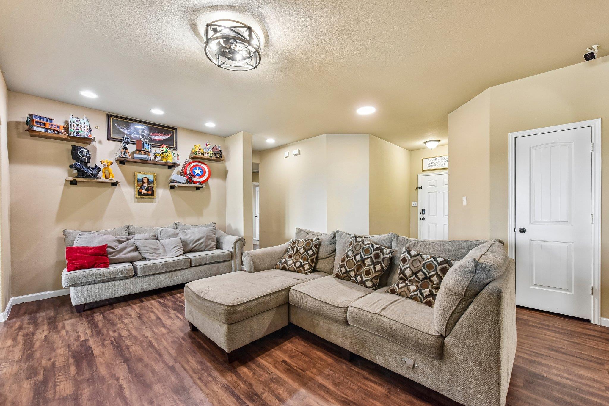 Living room with a gray sectional, wood-look floors, and collectible figures displayed on floating shelves.