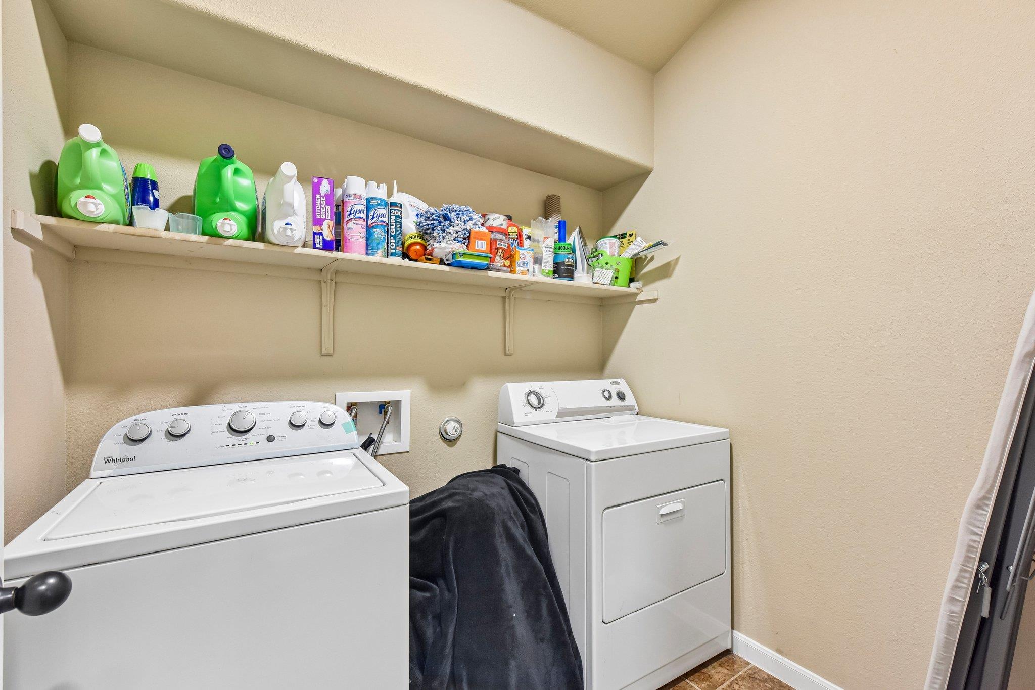 Laundry room with washer and dryer beneath a shelf of cleaning supplies.